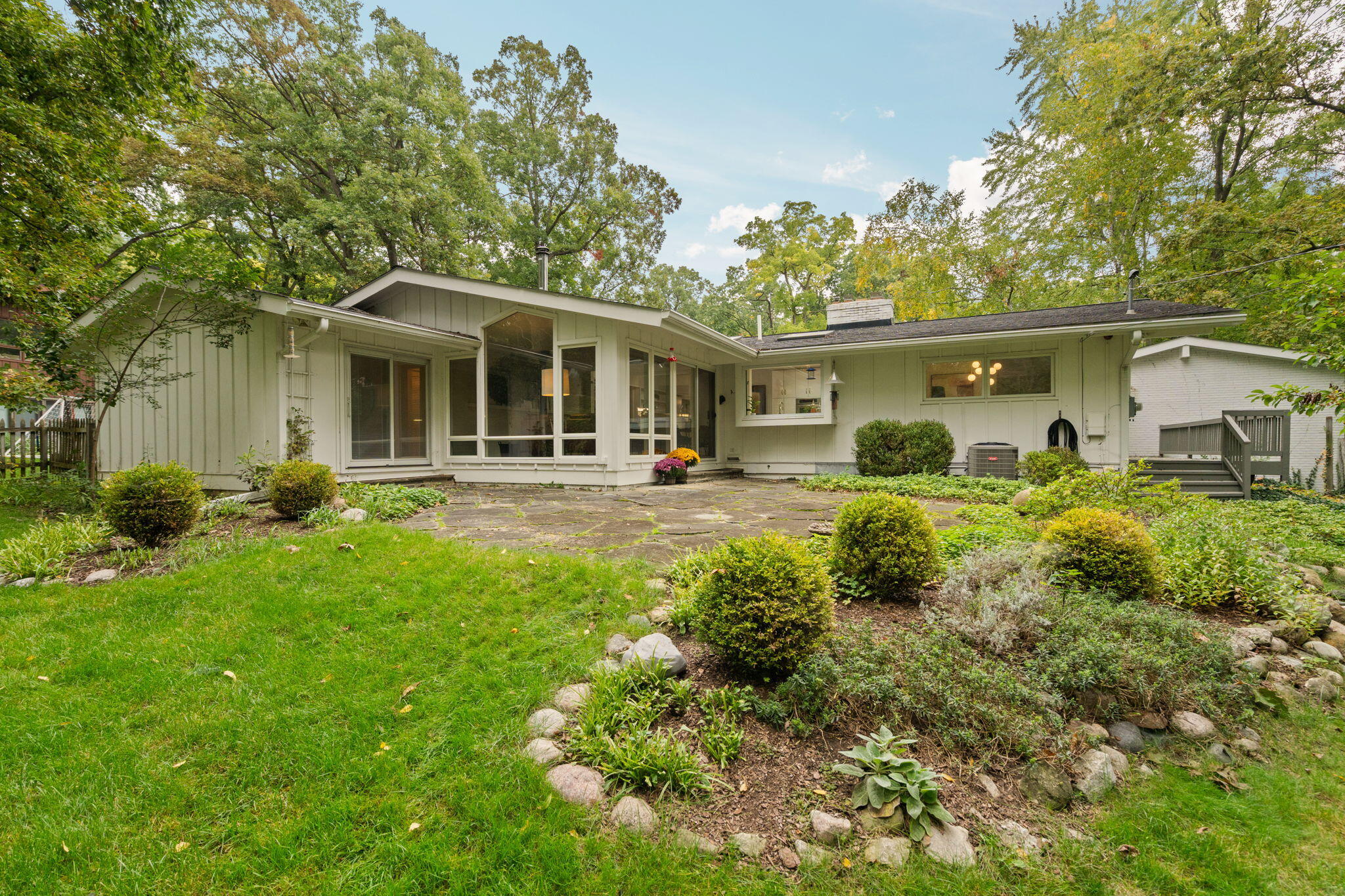 Single-story home with broad rear windows, stone patio, and landscaped yard beneath mature trees.