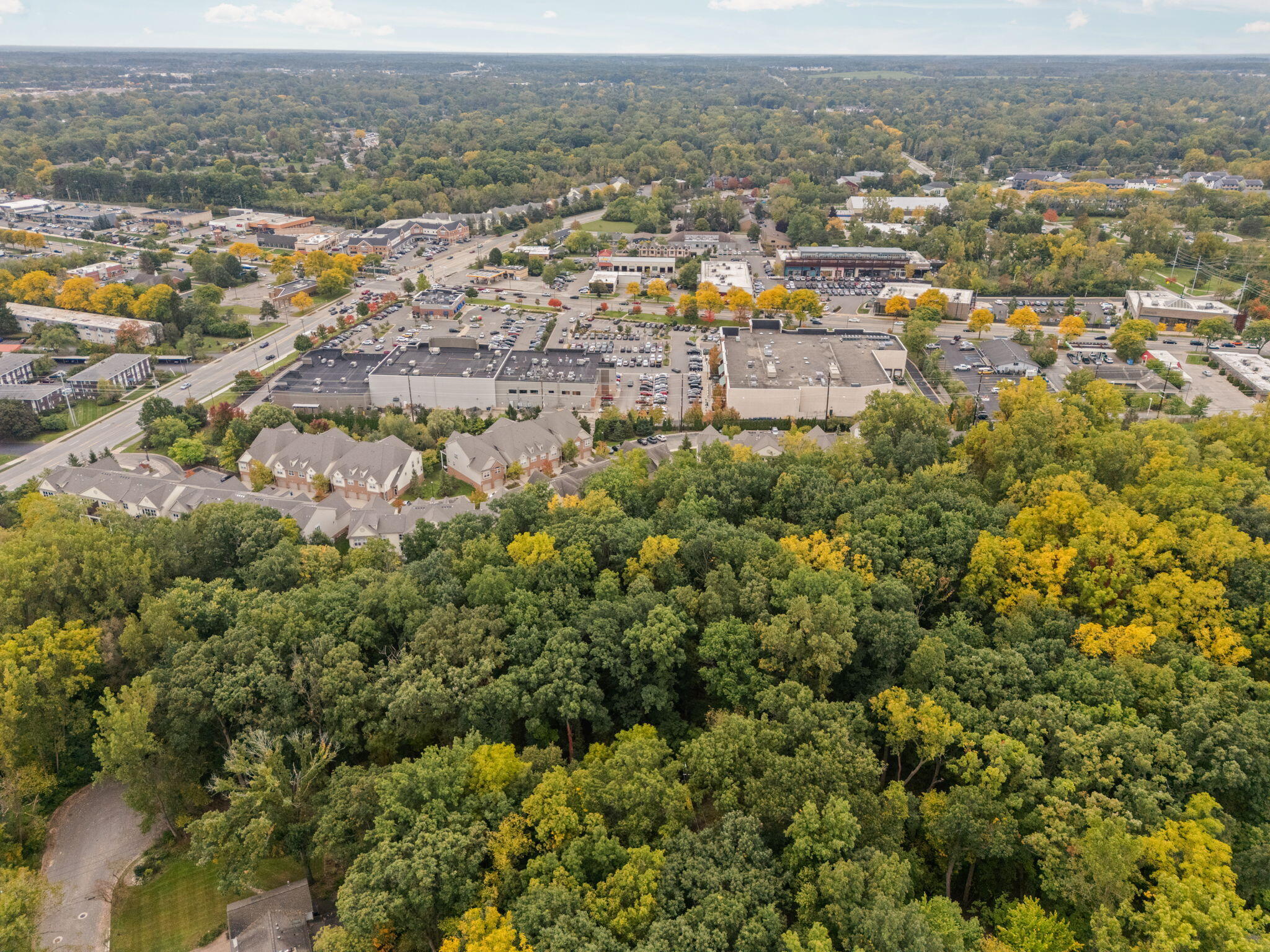 Aerial view of wooded homes beside a commercial district, with autumn-colored trees.