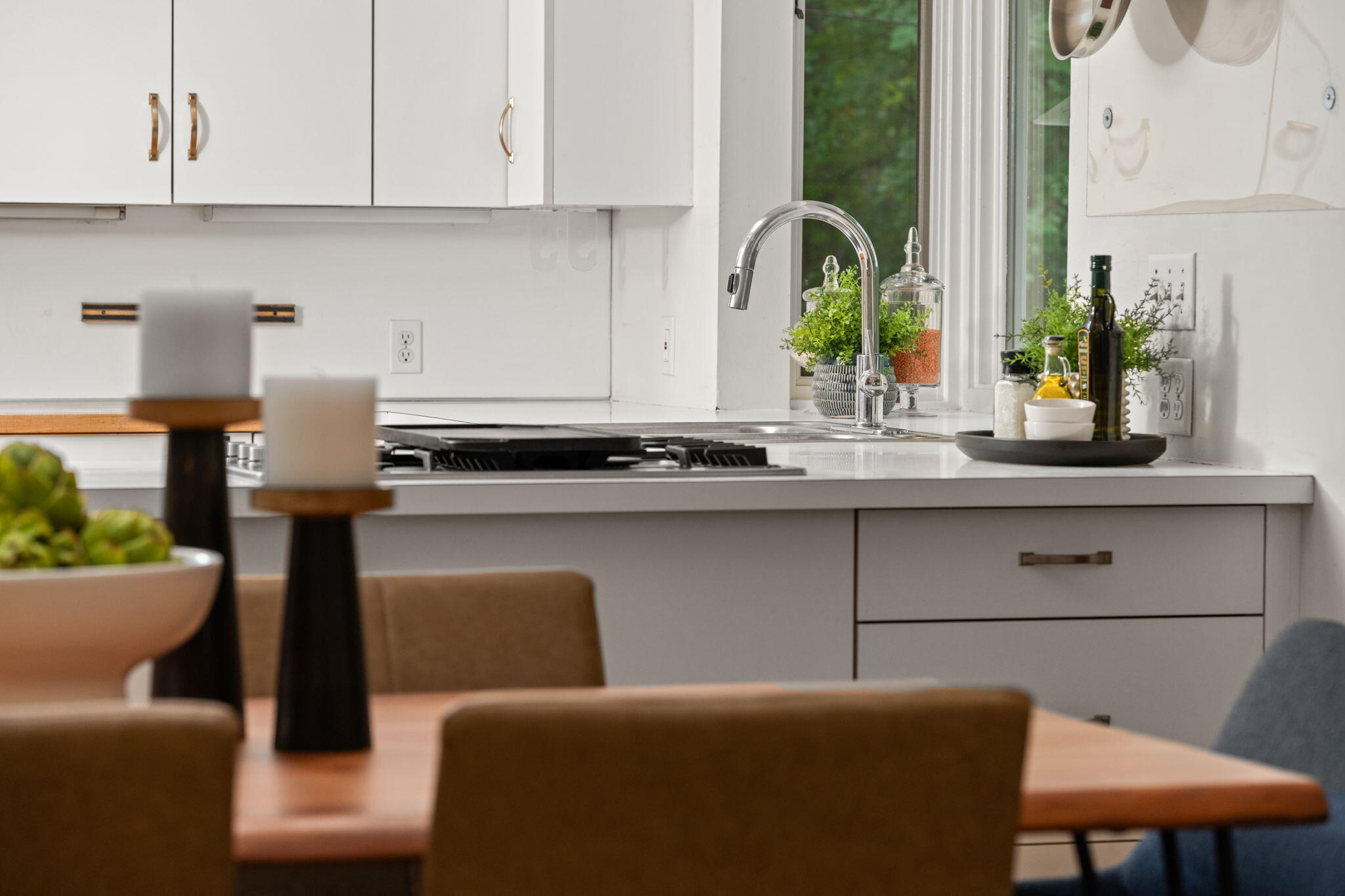 Bright white kitchen with a gooseneck faucet, gas cooktop, and dining table in the foreground.
