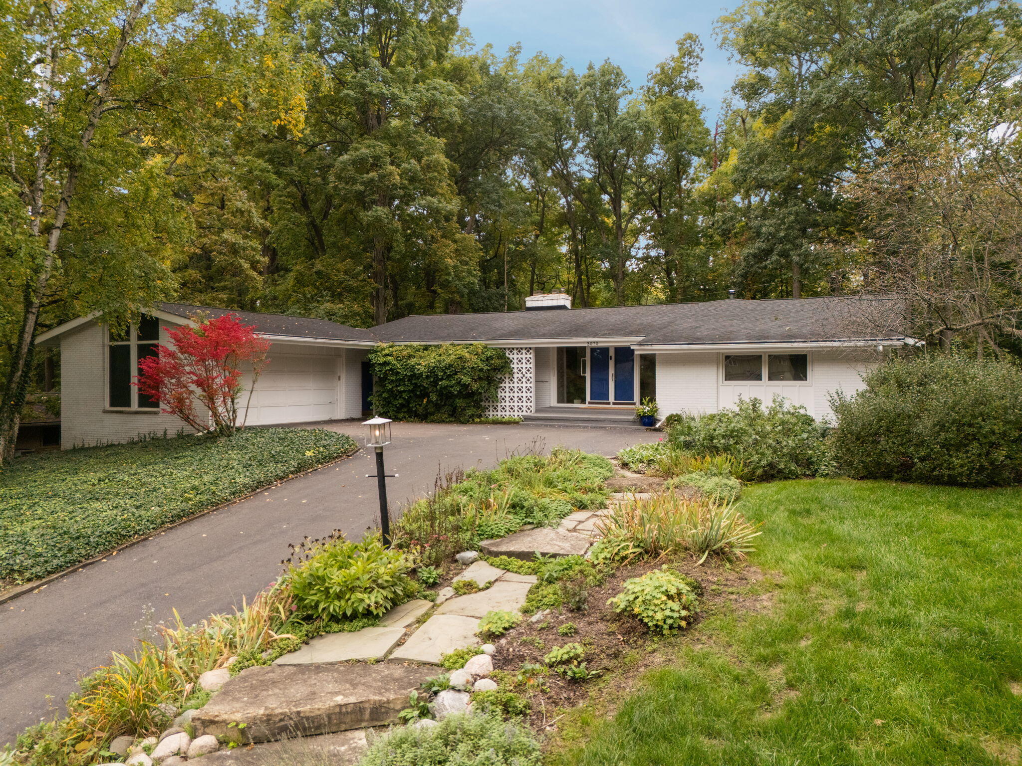 Single-story white home with blue entry doors, attached garage, and landscaped front garden.
