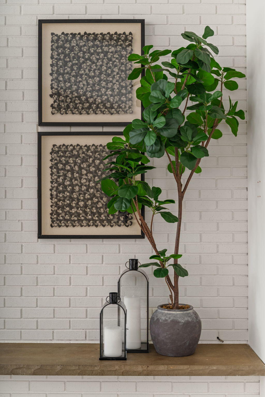 Leafy potted plant beside framed abstract art and candle lanterns on a stone ledge.