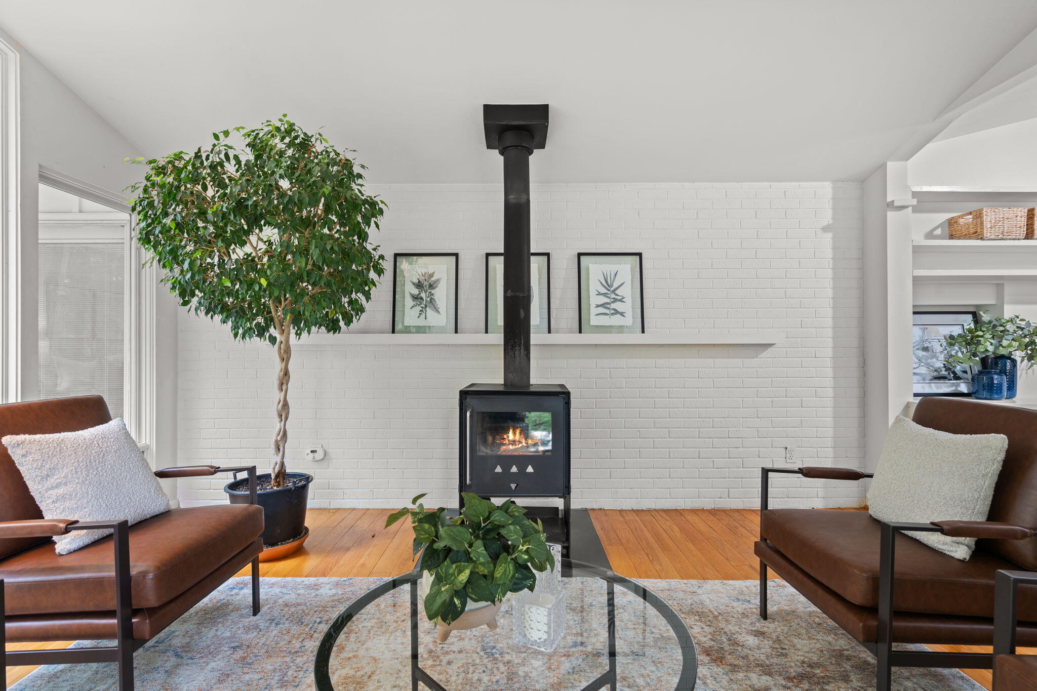 Living room with a black wood stove, white brick wall, and brown leather chairs.