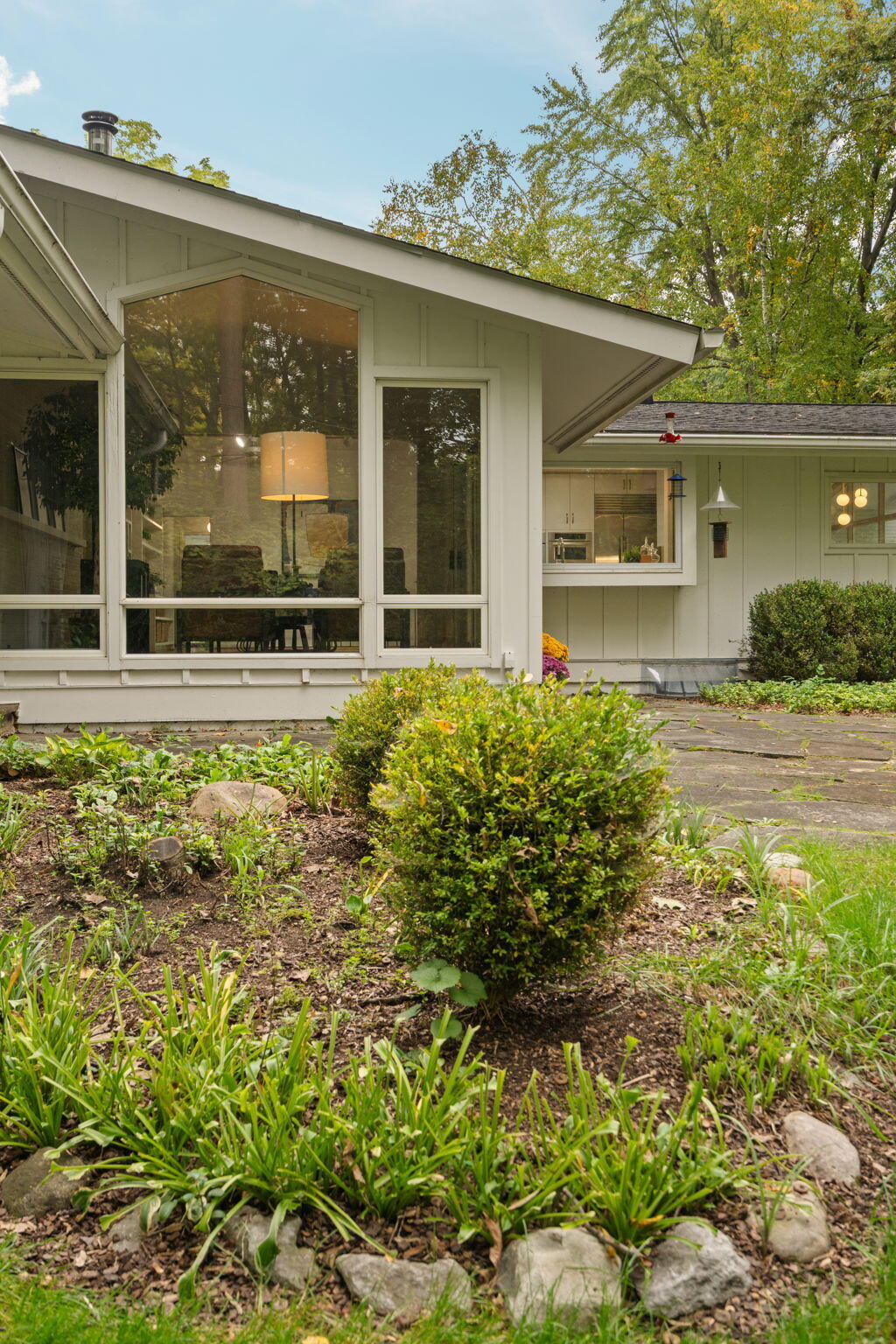 House with expansive windows overlooking a landscaped garden and stone patio.
