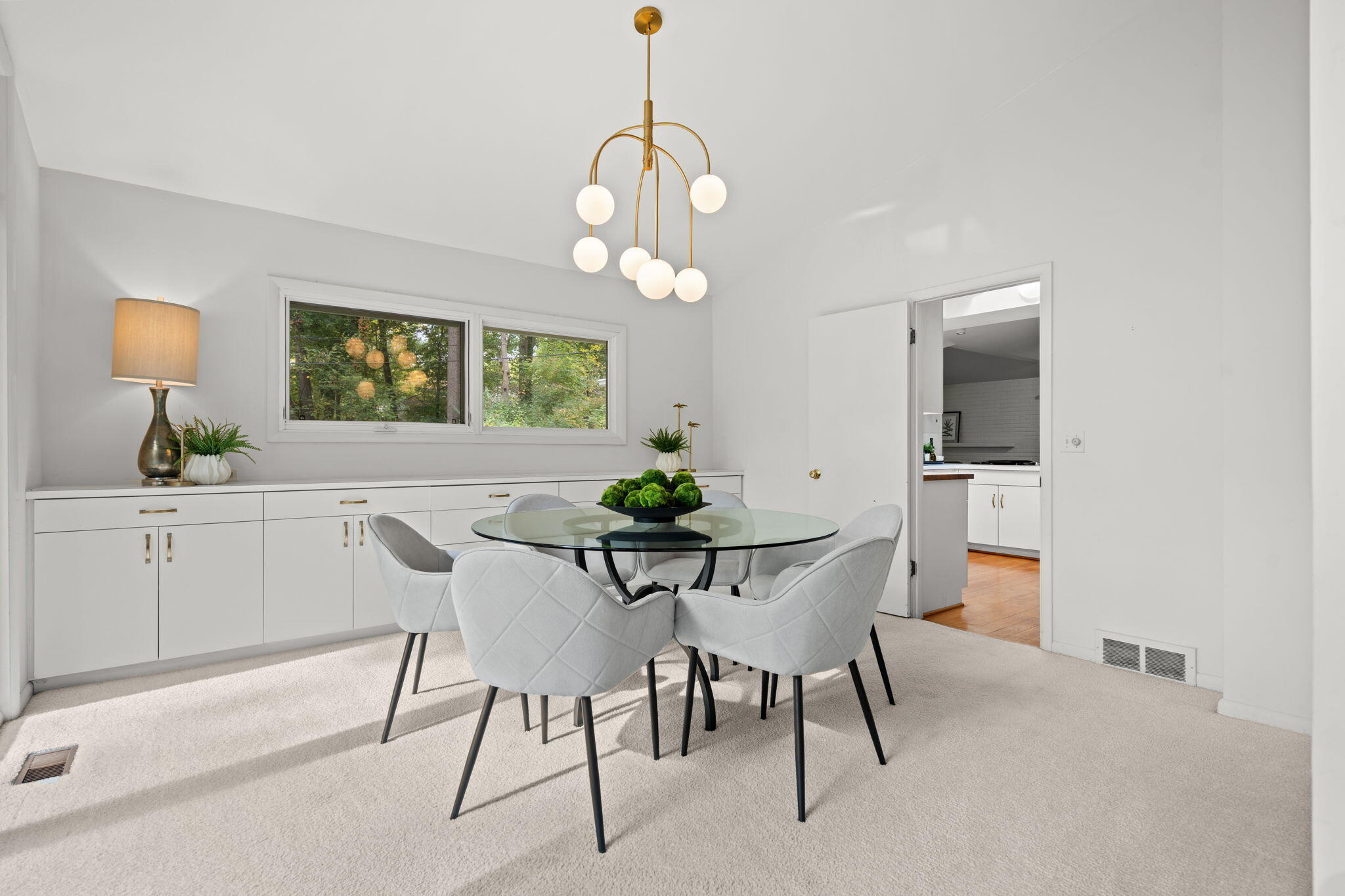 Furnished dining room with a glass table, gray chairs, brass chandelier, and built-in white cabinetry.