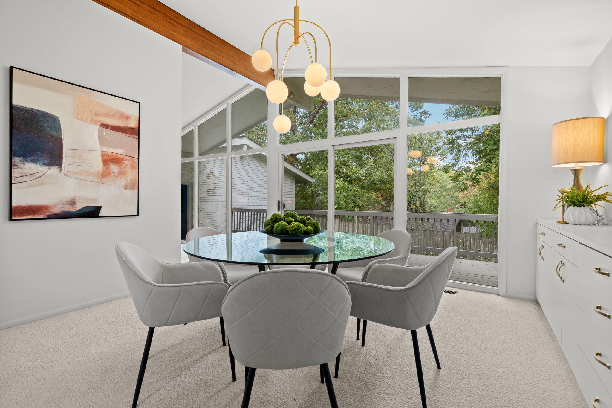 Dining room with a glass table, globe chandelier, and large windows overlooking a leafy deck.