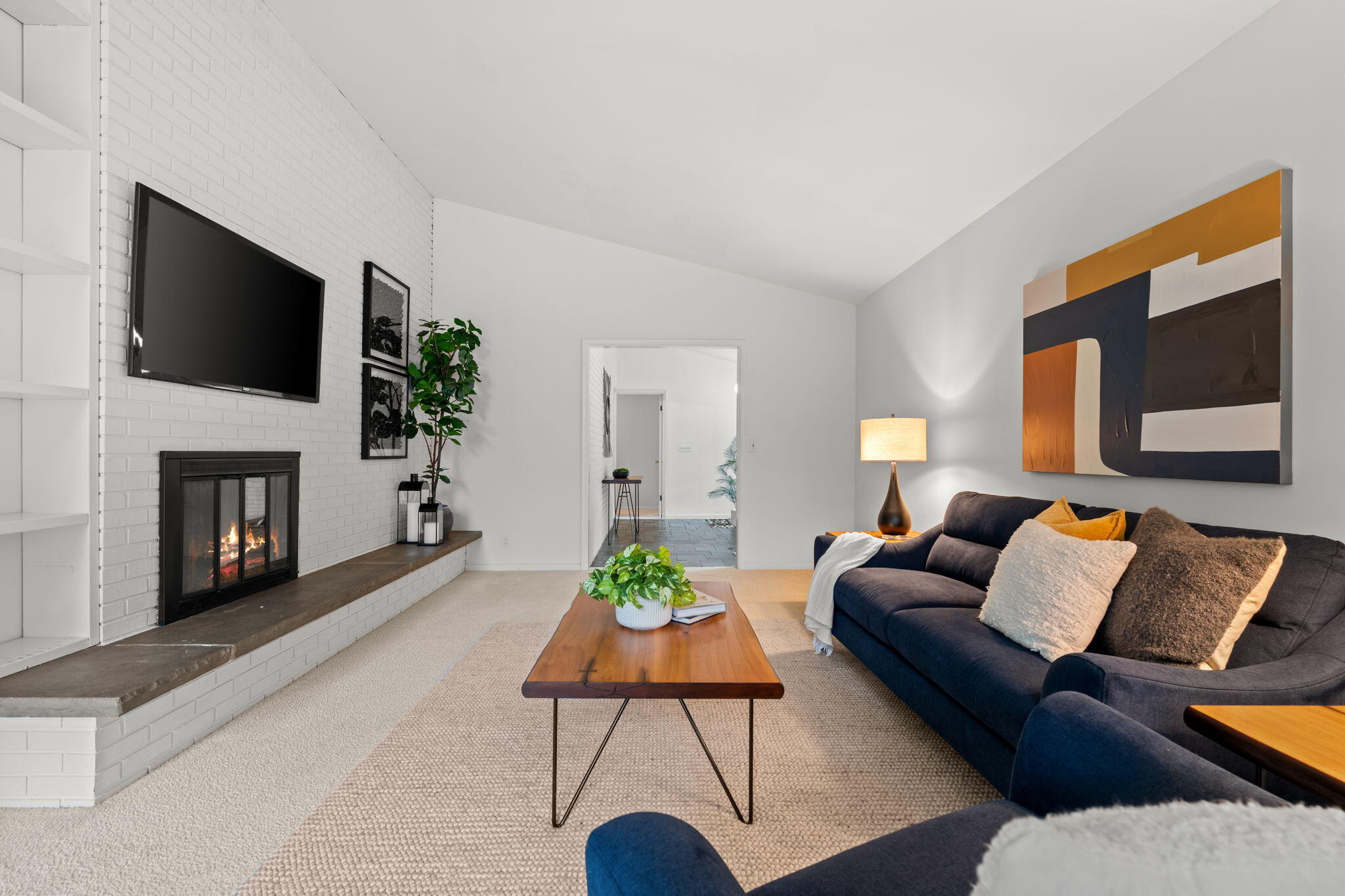 Living room with a blue sectional, white brick fireplace, and large abstract artwork.