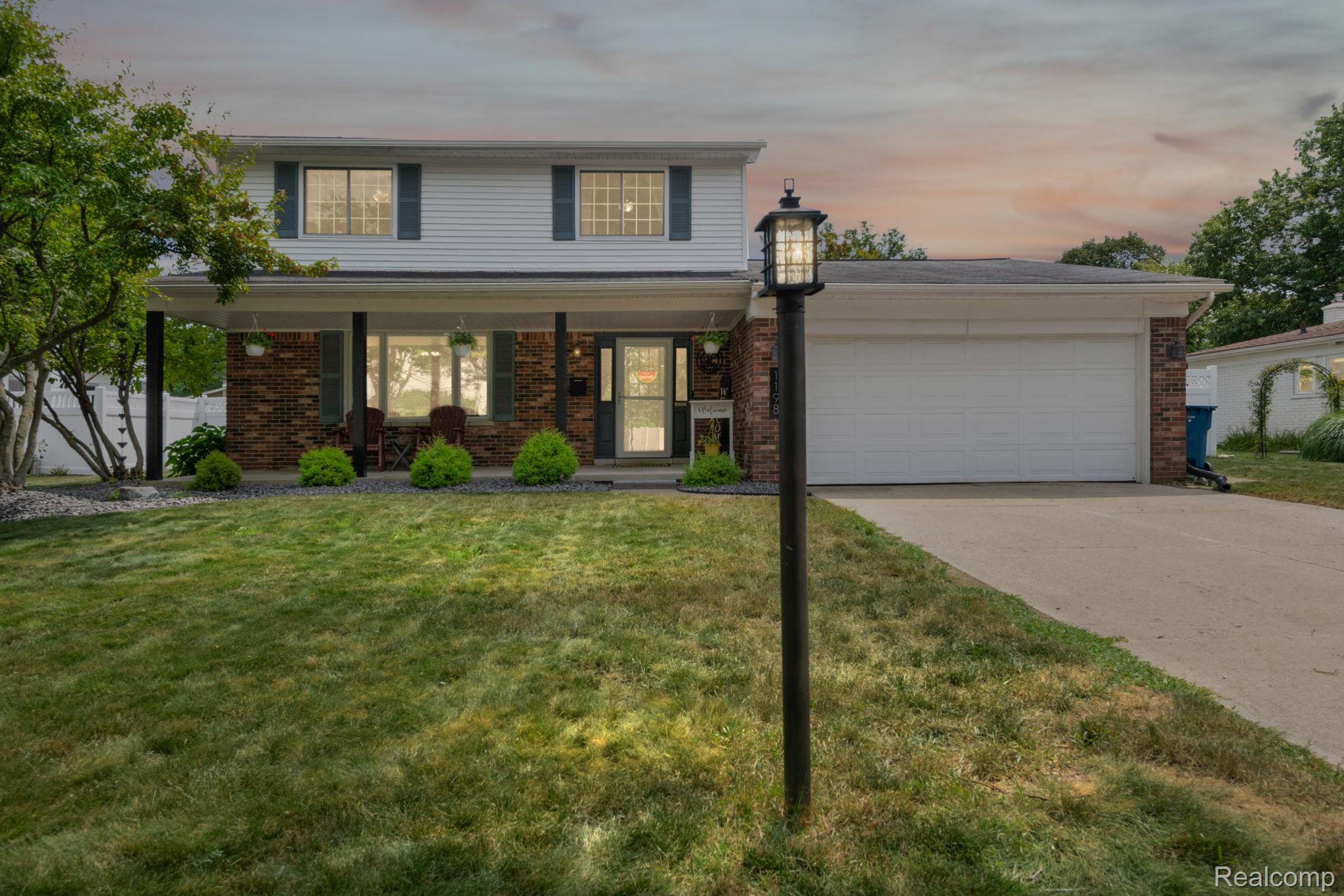 Two-story brick-and-siding home with a covered porch, attached garage, and illuminated lawn lamp.