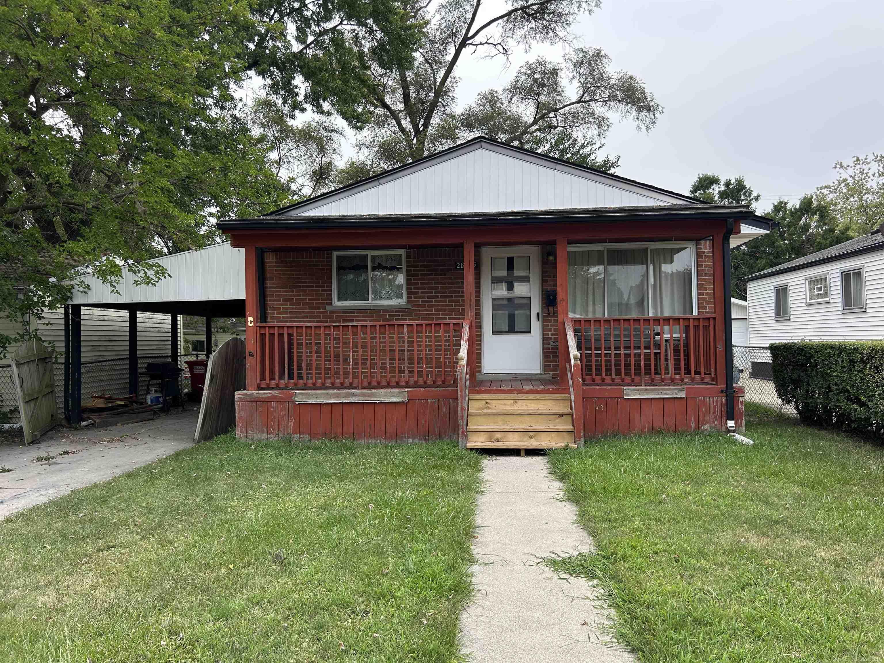 Brick house with a red-railed porch, new wooden steps, and a white carport.