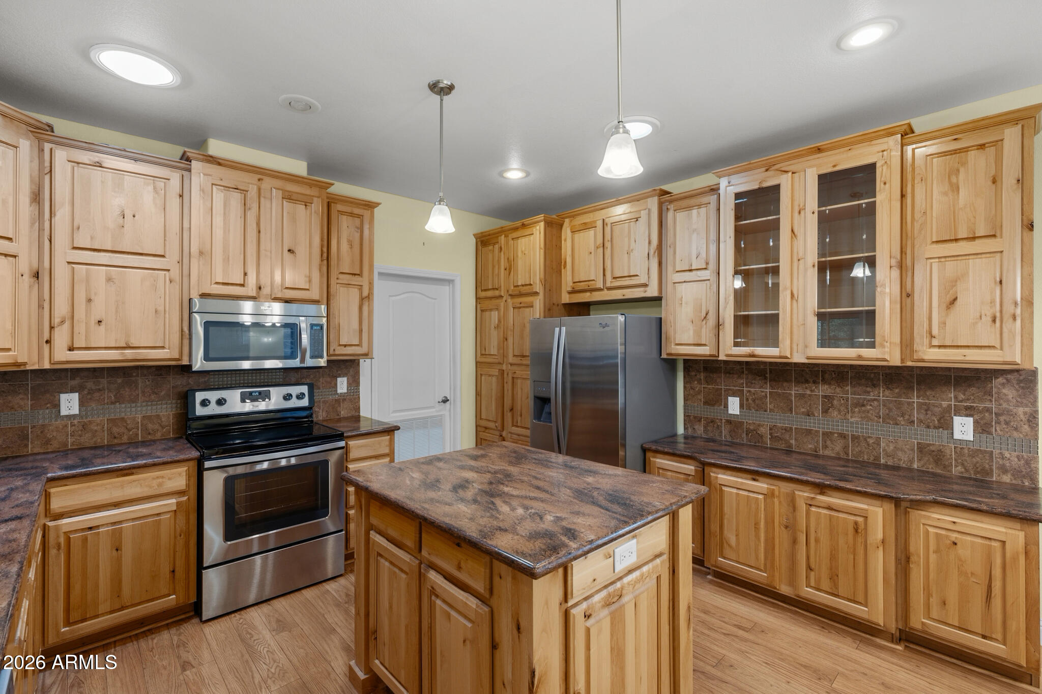 Kitchen with wood cabinets, a central island, stainless steel appliances, and brown tile backsplash.