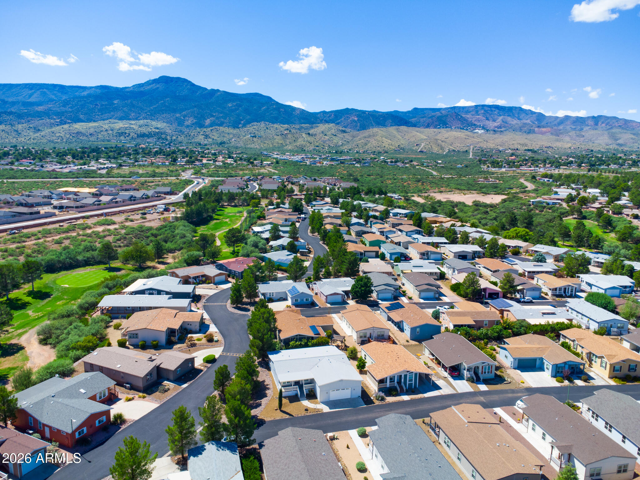 Aerial view of a residential neighborhood with a golf-course green and mountain range beyond.