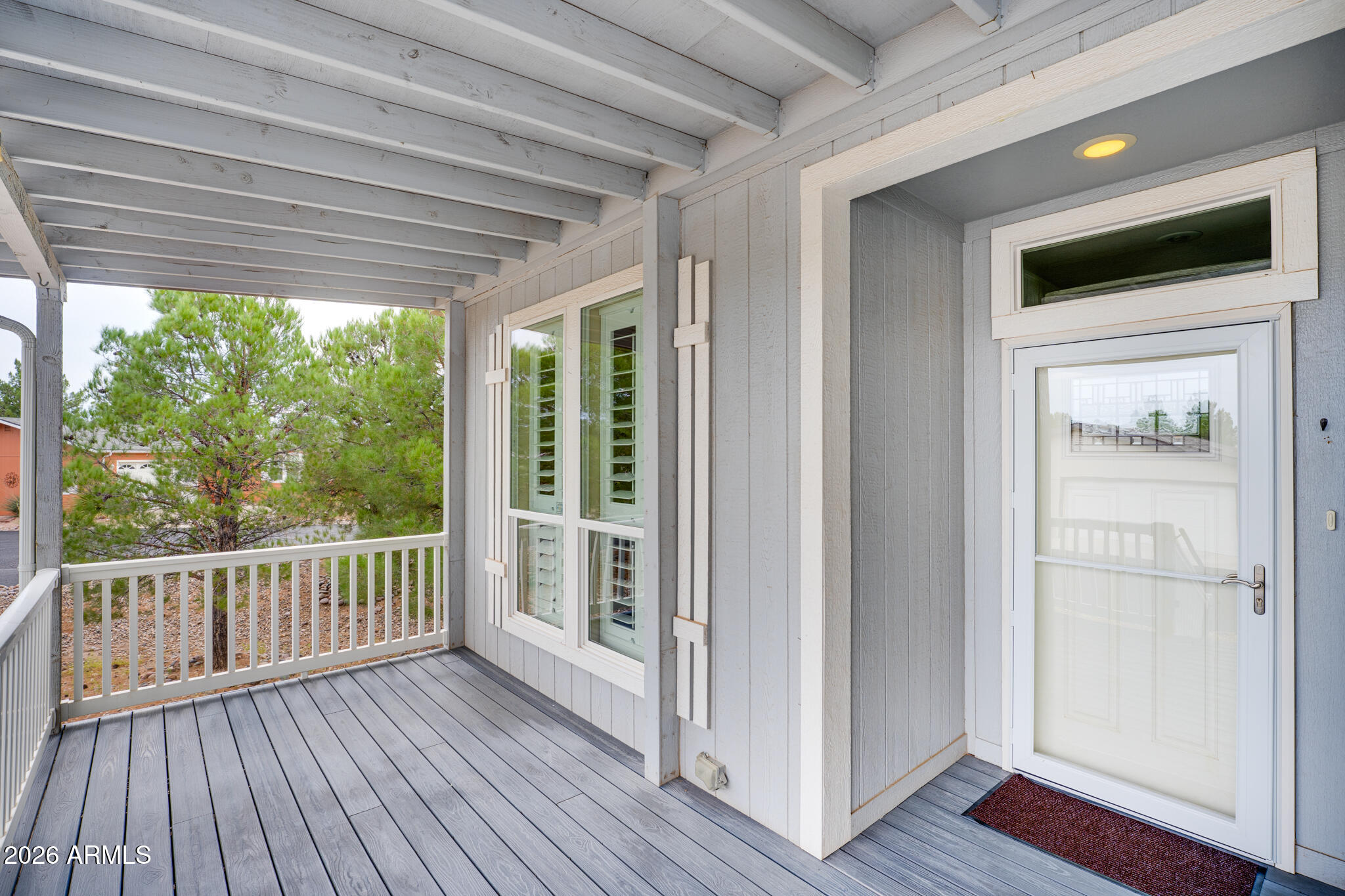 Covered porch with gray decking, white railing, shuttered windows, and a glass-paneled front door.