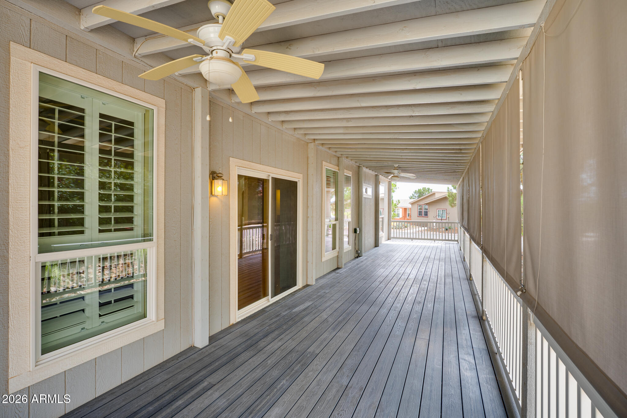 Long covered porch with gray decking, white railings, ceiling fan, shuttered windows, and sliding glass doors.