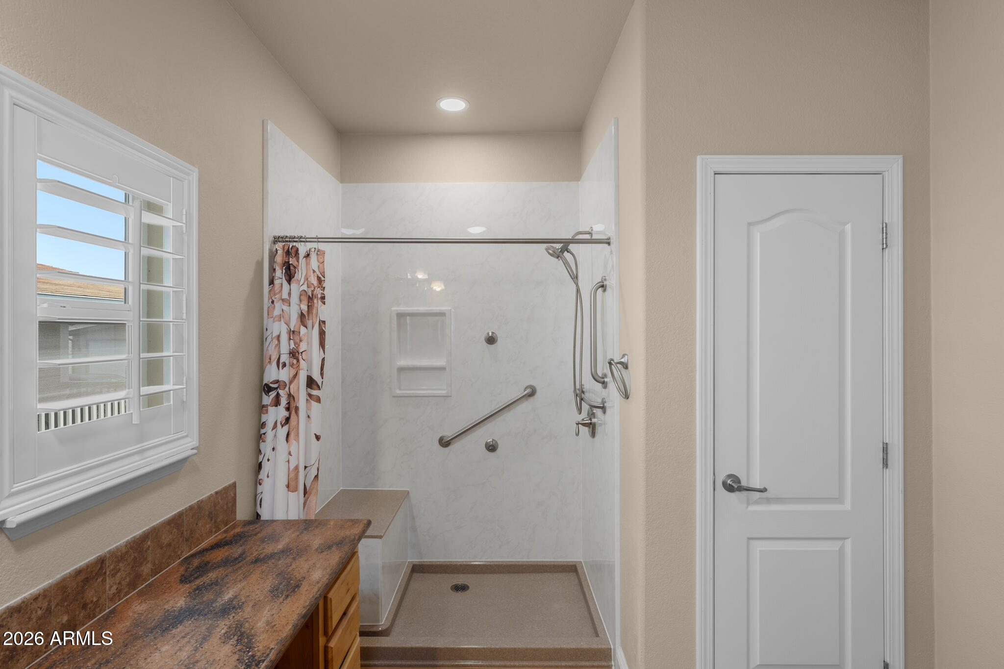Bathroom with a walk-in shower, grab bars, built-in seat, patterned curtain, and wood vanity counter.
