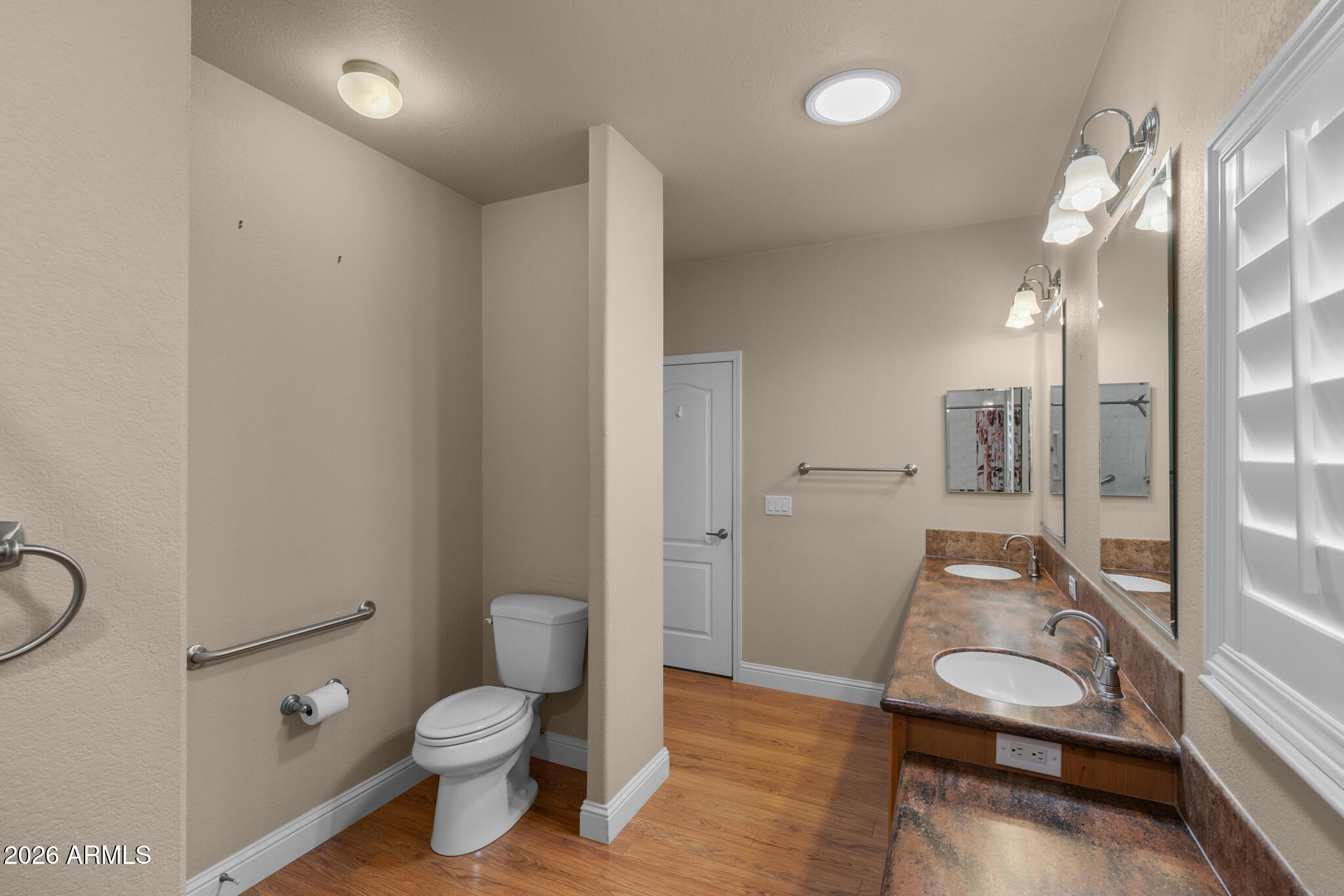 Bathroom with a double-sink vanity, large mirrors, and a toilet behind a partial wall.