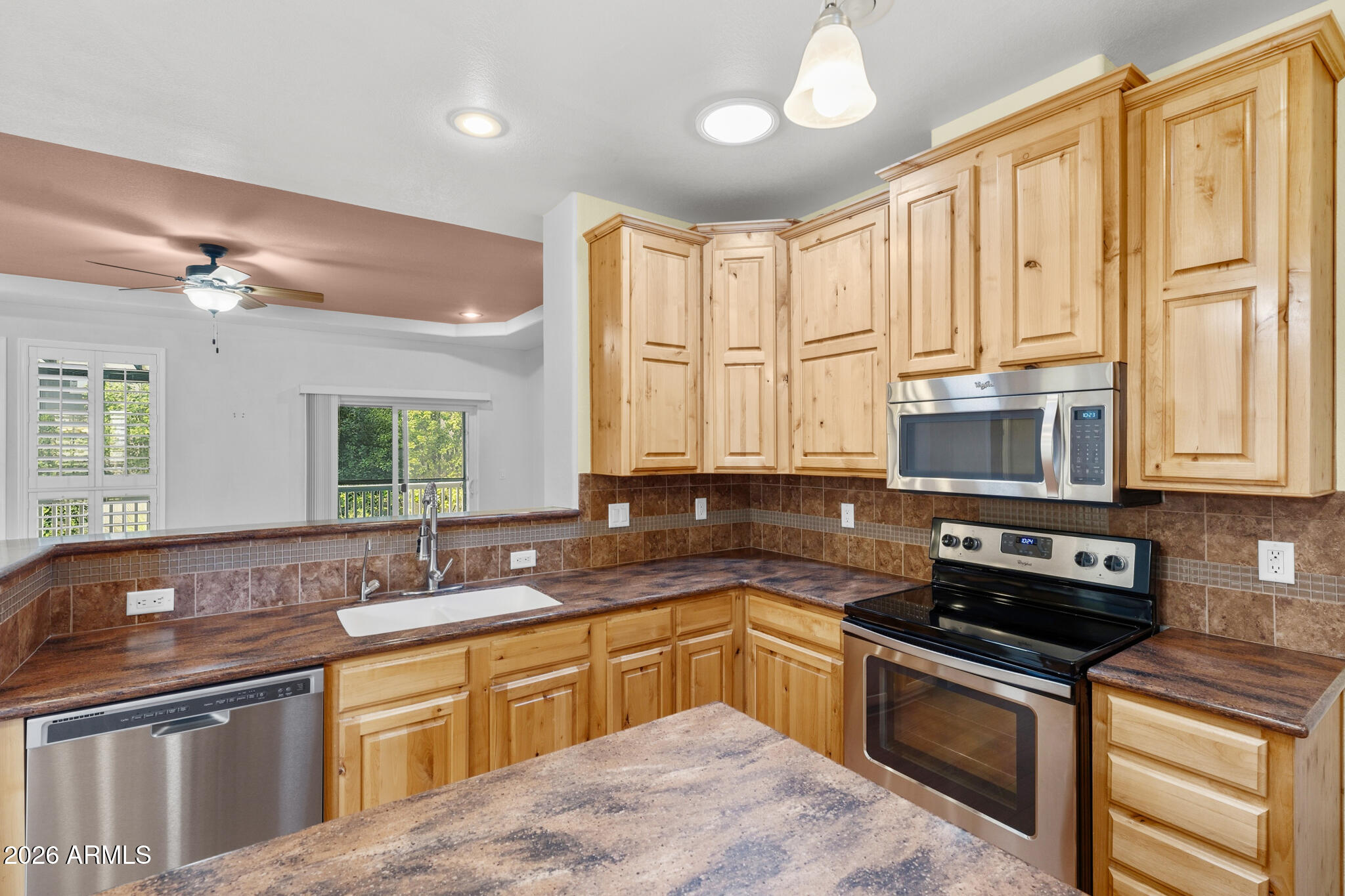 Kitchen with honey-toned cabinets, brown tile backsplash, and stone counters opening to a living area.