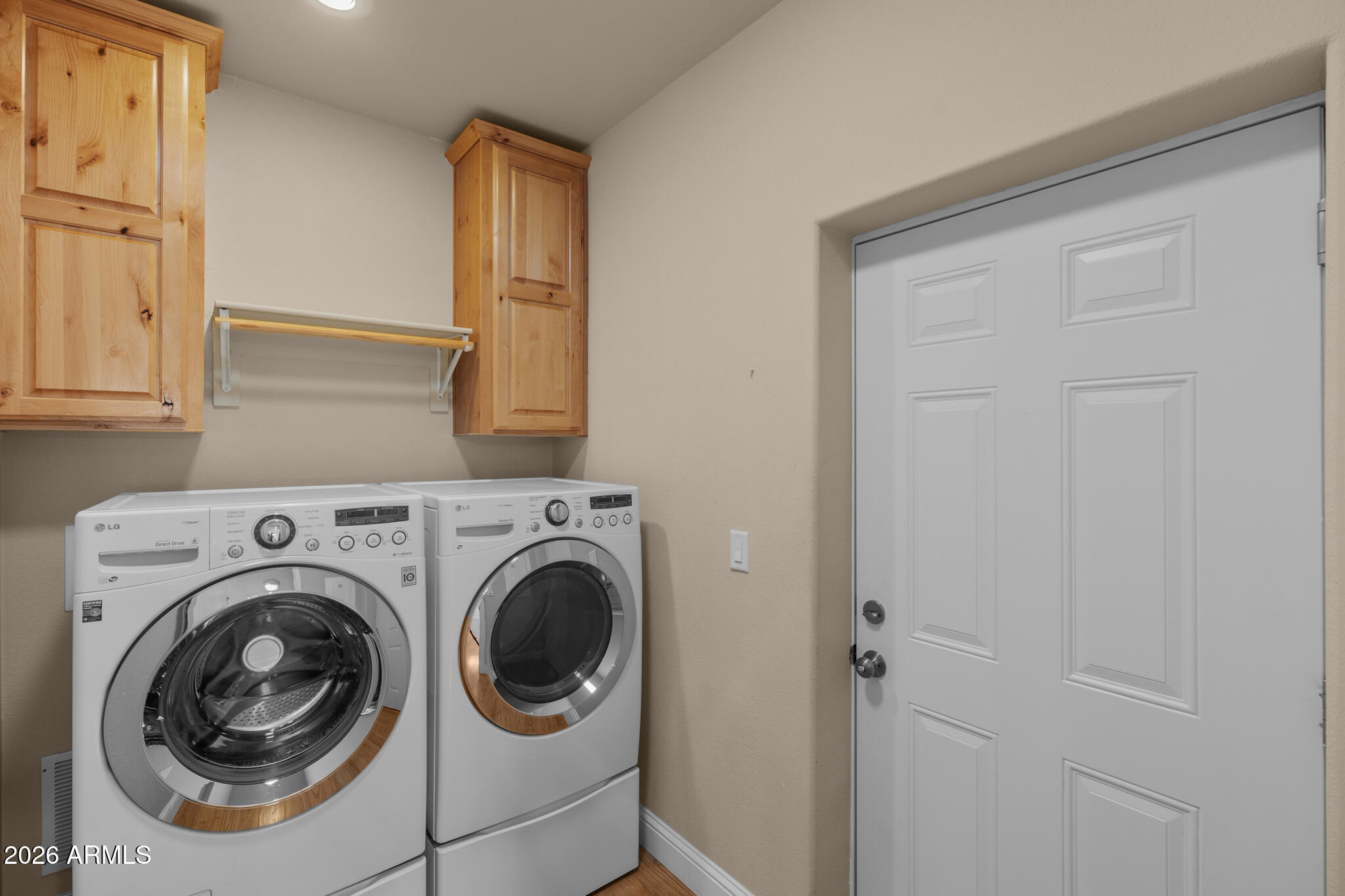 Laundry room with front-loading washer and dryer beneath pine cabinets beside a white paneled door.
