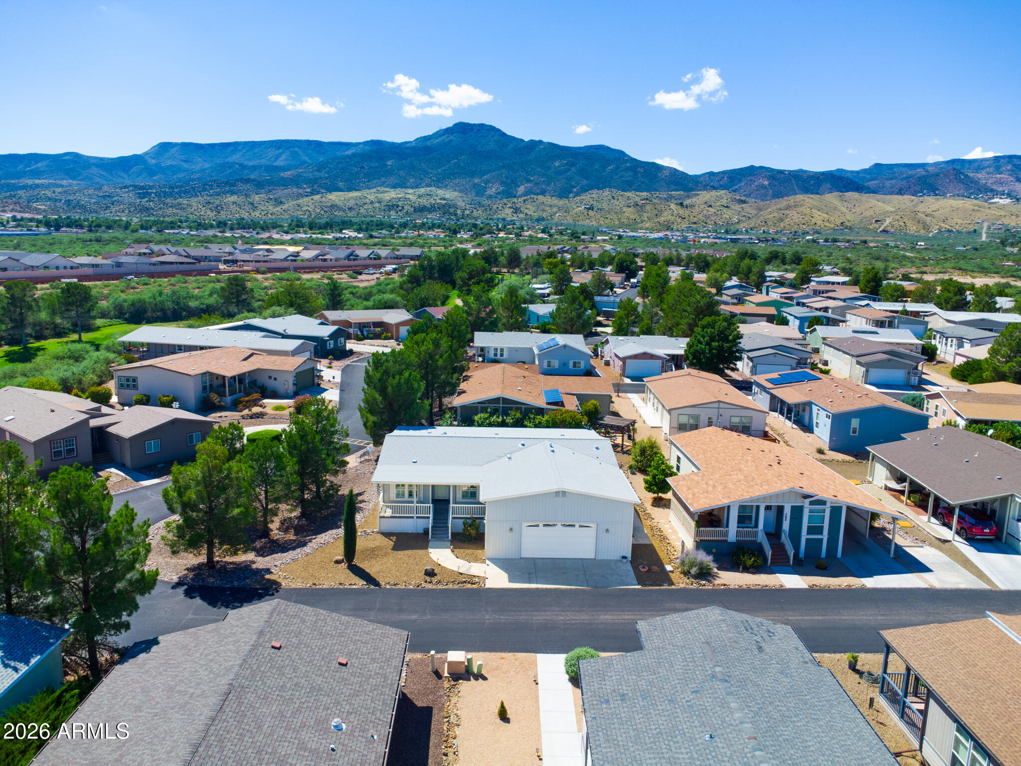 Aerial view of a light-colored home among neighborhood houses, with mountains in the distance.