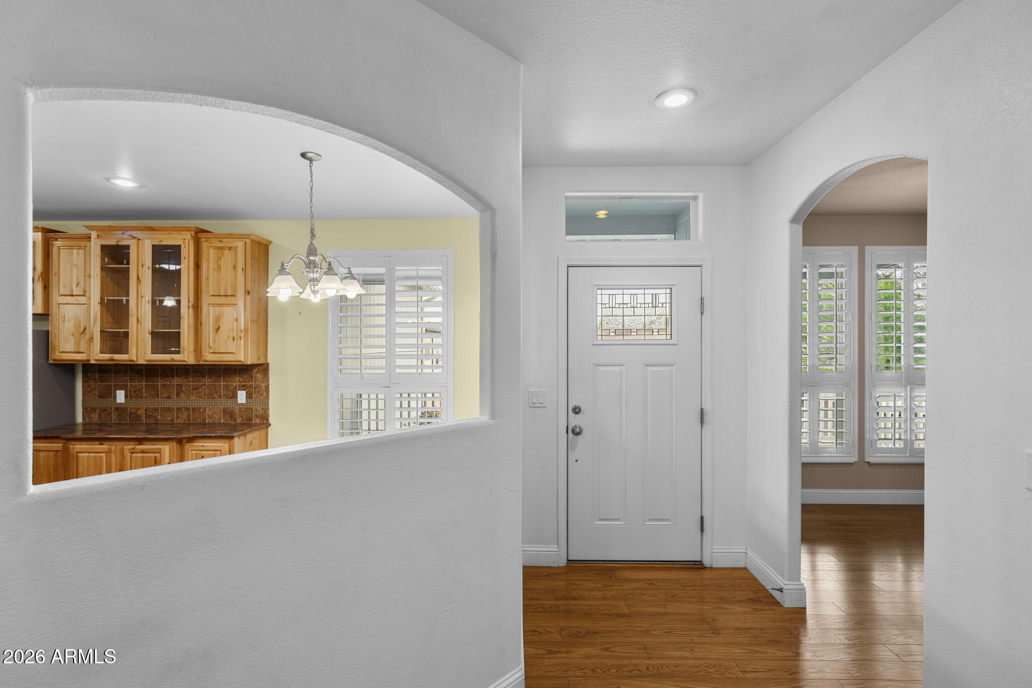 Entryway with a white front door, arched openings, wood floors, and a kitchen with wood cabinetry.