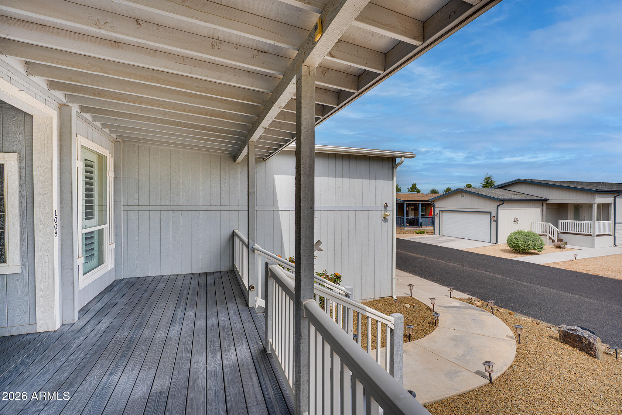 Covered porch with gray decking and white railings overlooking neighboring homes and a gravel yard.