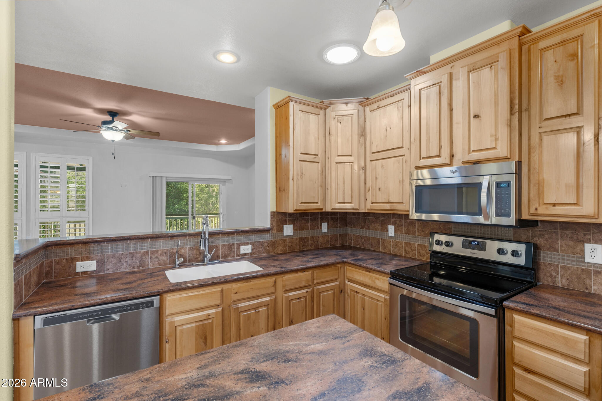 Kitchen with honey-colored wood cabinets, brown tile counters, stainless appliances, and a breakfast bar overlooking the living area.