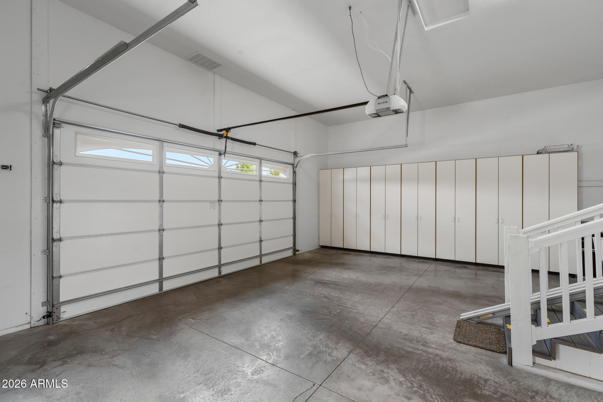 Empty garage with a windowed overhead door, built-in cabinets, and concrete flooring.