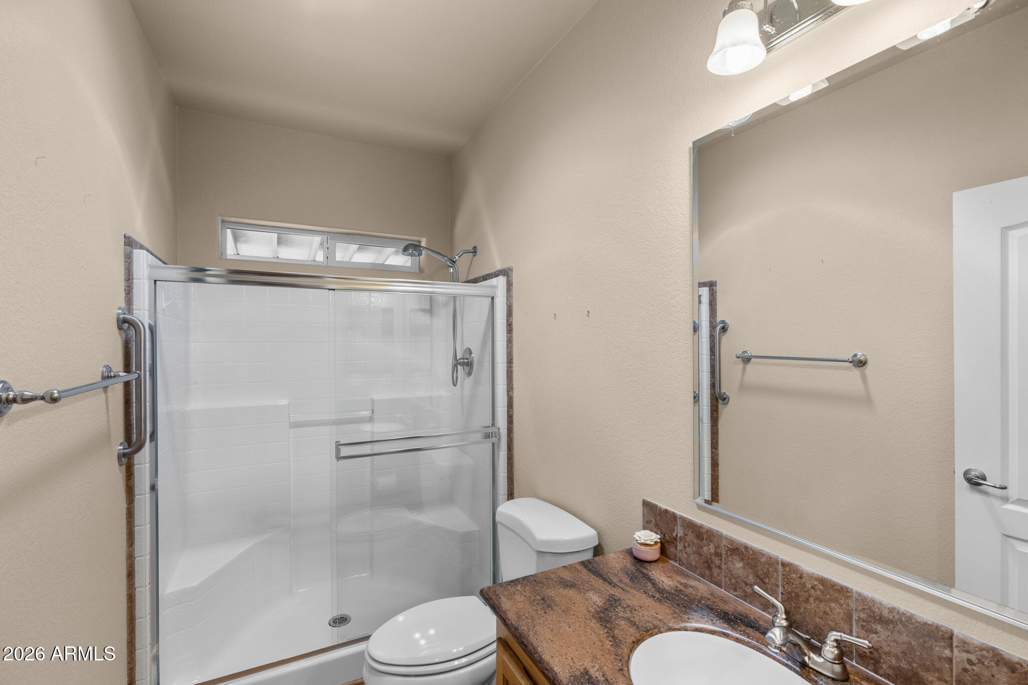 Bathroom with a glass-enclosed shower, grab bars, and a brown stone vanity countertop.