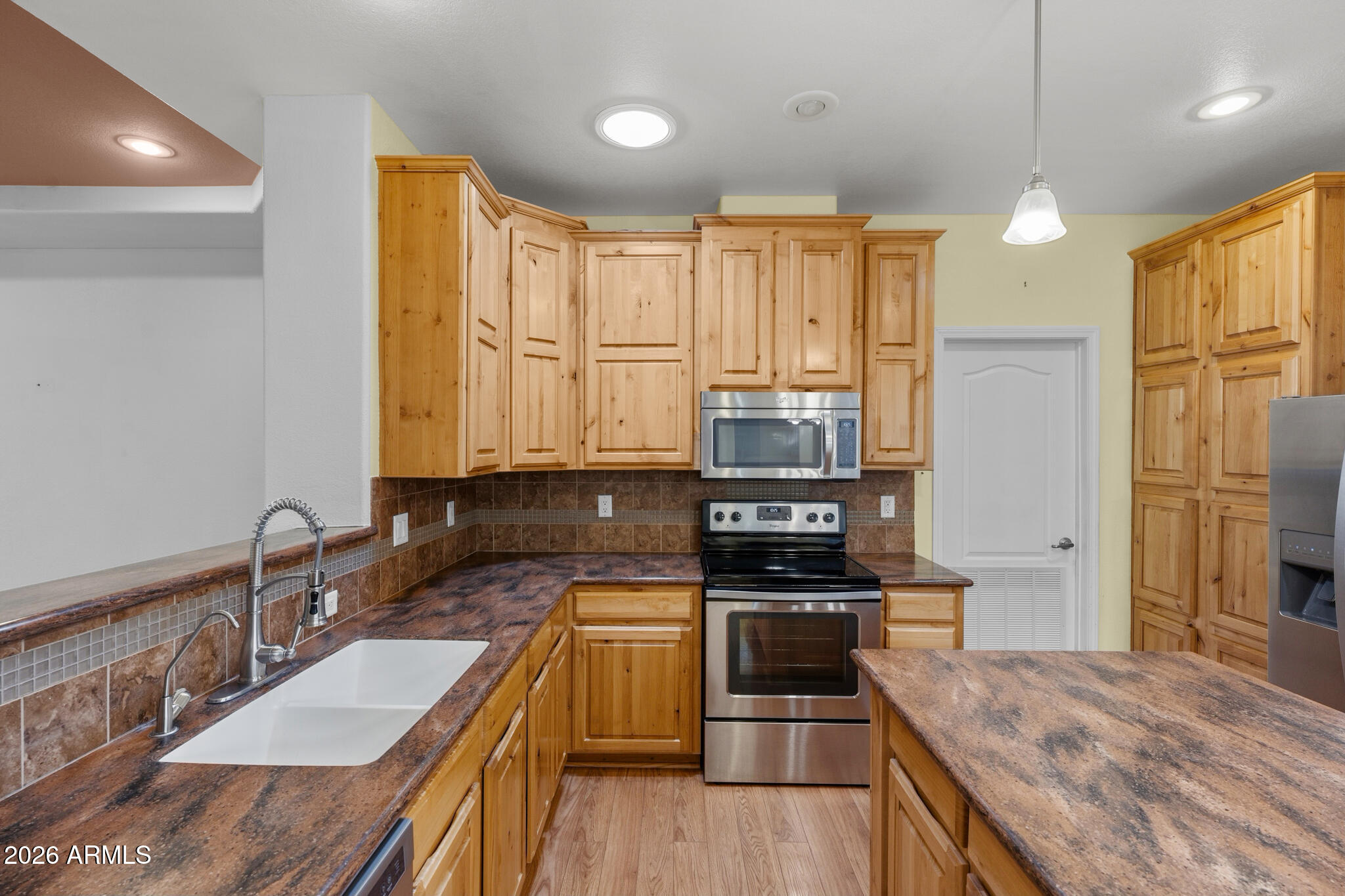 Kitchen with honey-toned cabinets, mottled counters, a white double sink, and stainless steel appliances.
