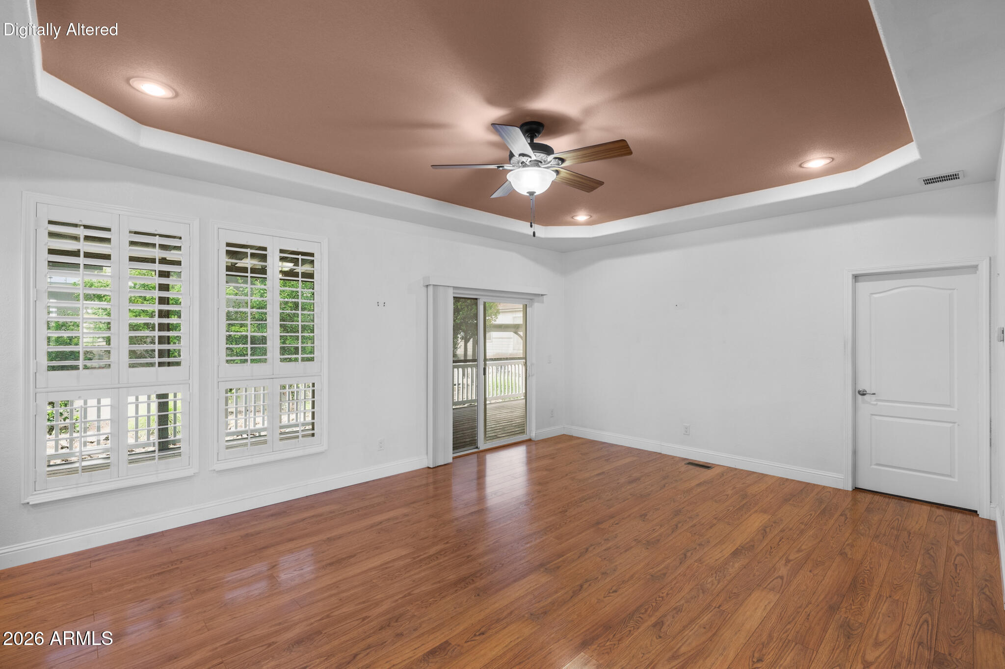 Empty room with hardwood floors, plantation shutters, a tray ceiling, and sliding glass door to a deck.