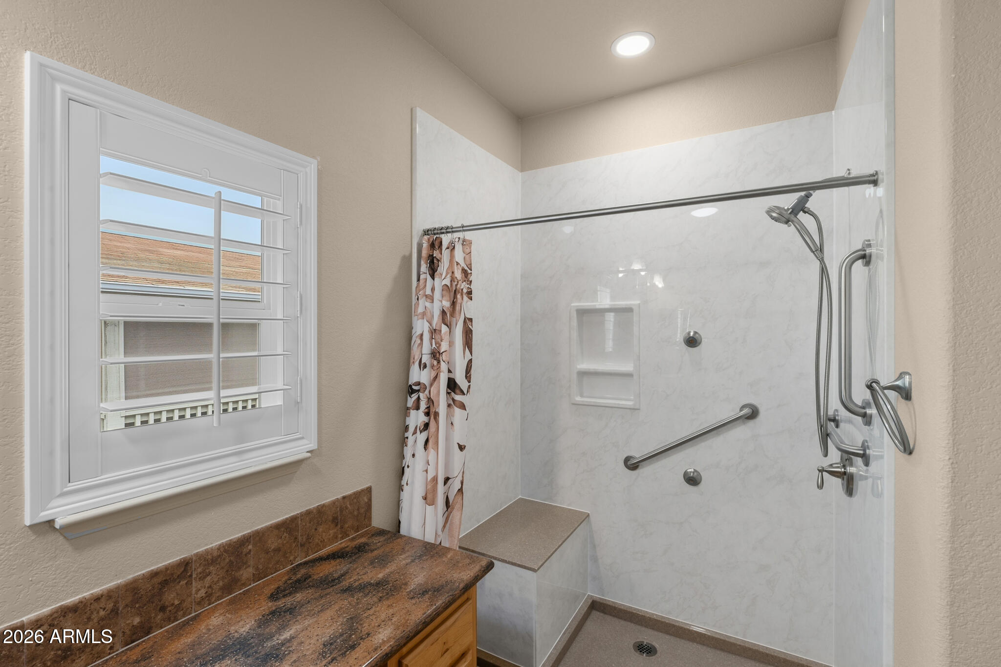 Bathroom with a marble-look walk-in shower, built-in seat, grab bars, and shuttered window.