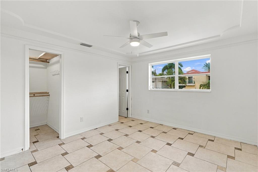 Empty bedroom with tiled floor, ceiling fan, and open closet.