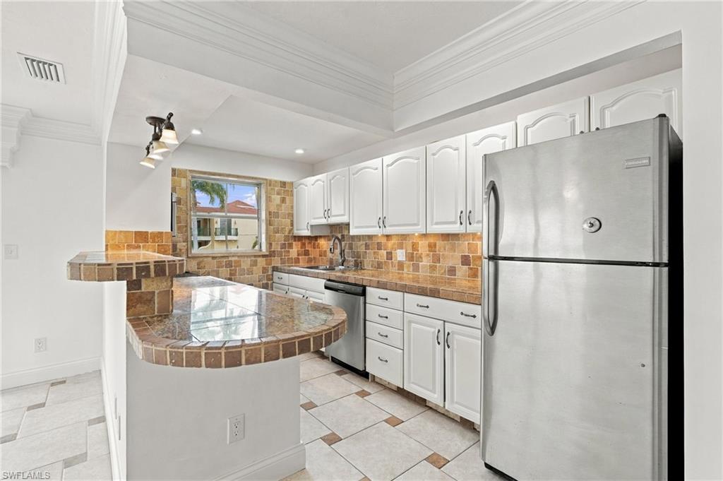 Kitchen with white cabinets, stainless appliances, tan tile counters, and a curved breakfast bar.
