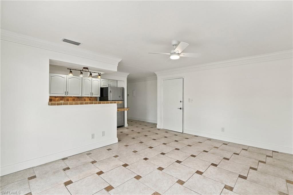 Empty tiled living area adjoining a compact kitchen with white cabinets and stainless steel appliances.