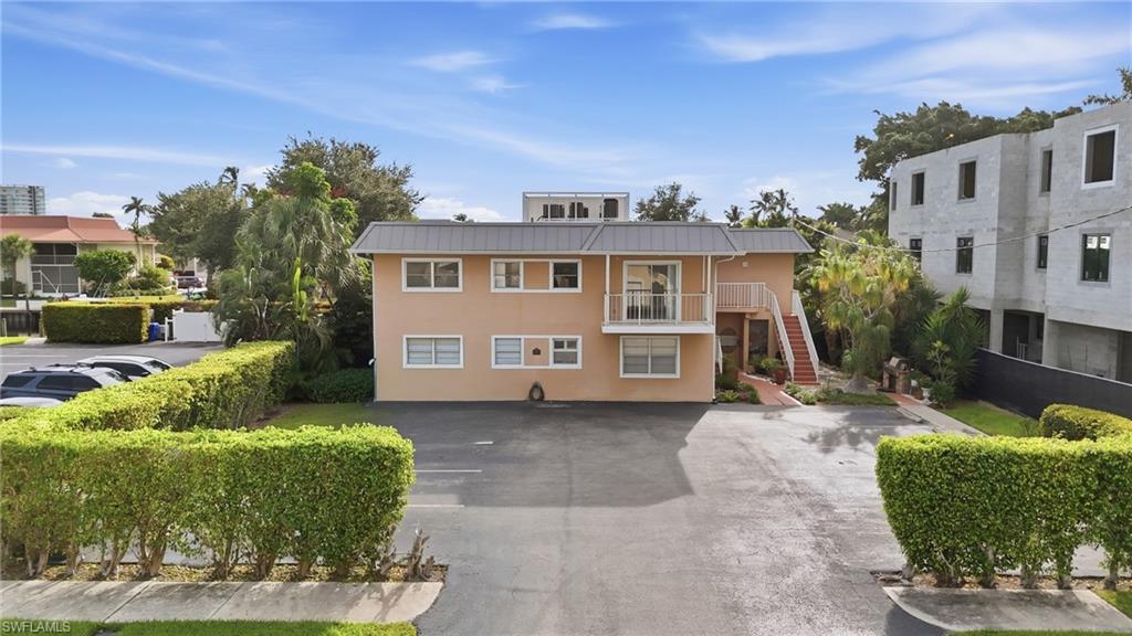Two-story peach building with a central balcony, exterior stairs, parking area, and tropical landscaping.