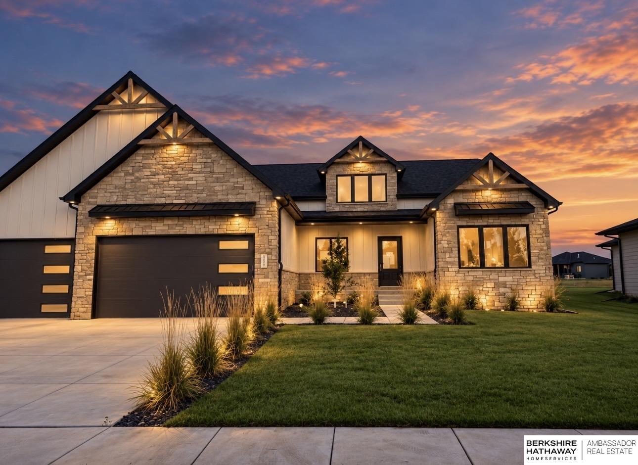 Stone-and-siding home with a double garage and illuminated landscaping at sunset.