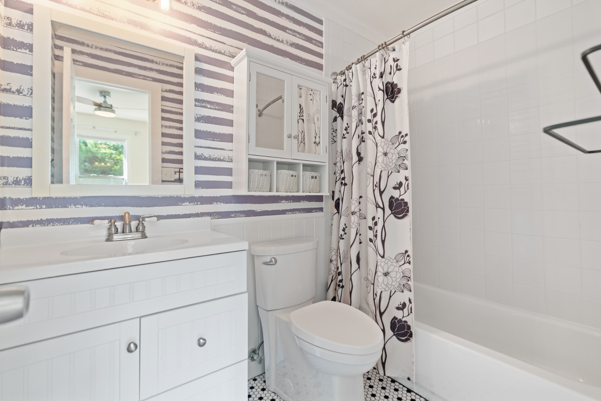 Bathroom with a white vanity, striped walls, mirrored storage cabinet, and floral shower curtain.