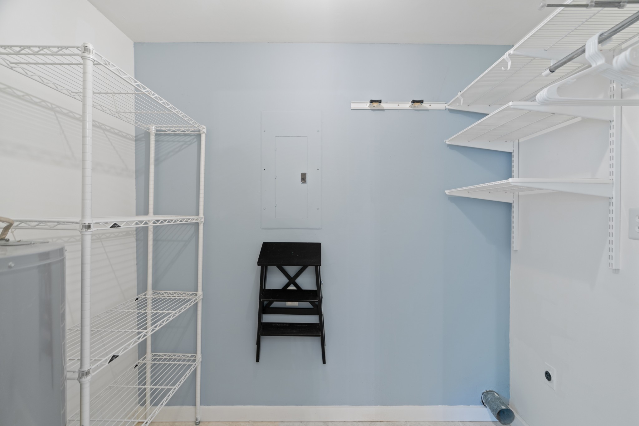 Walk-in closet with white wire shelving, hanging rails, and a black step stool.