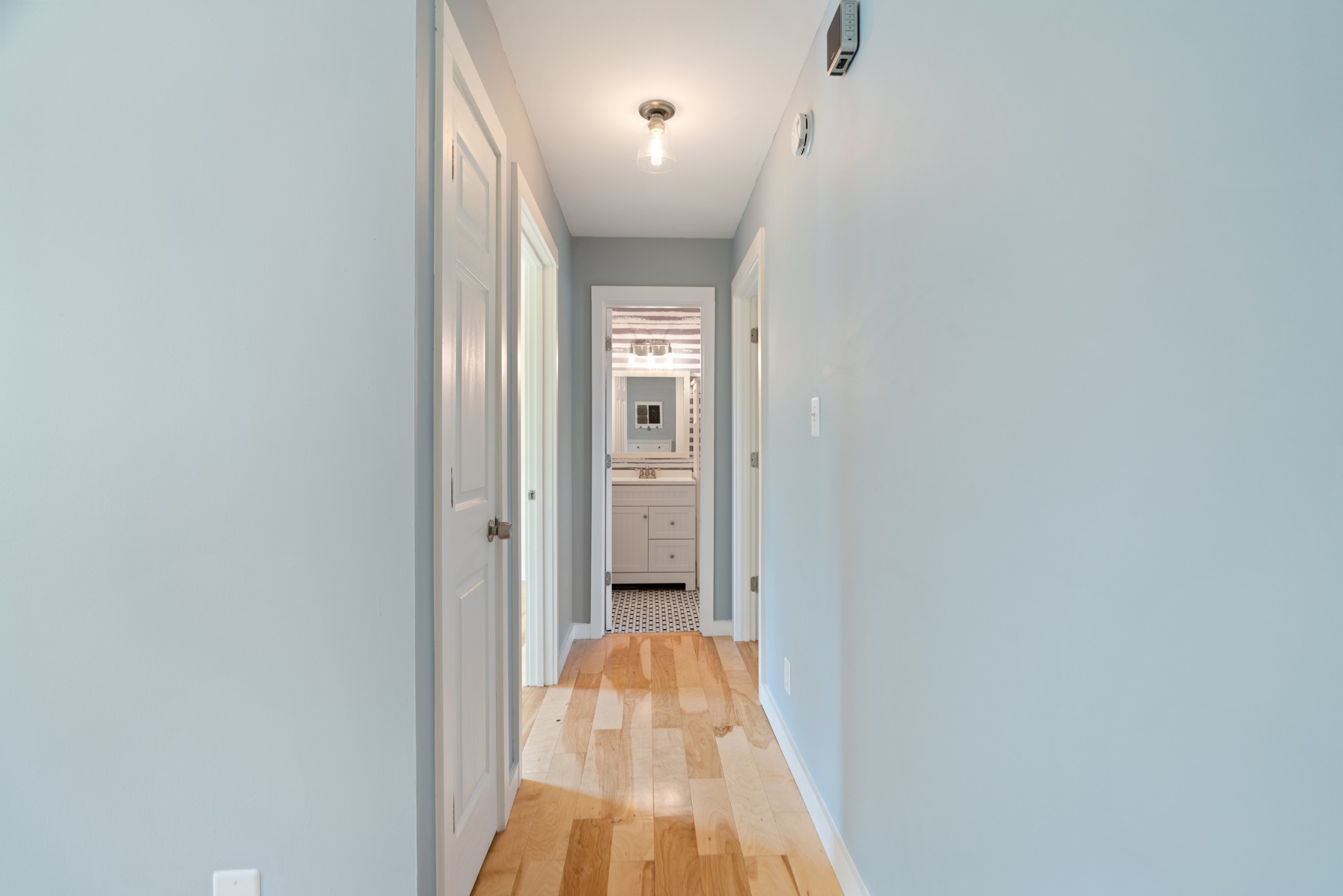 Hallway with warm wood floors leading to a bathroom vanity.