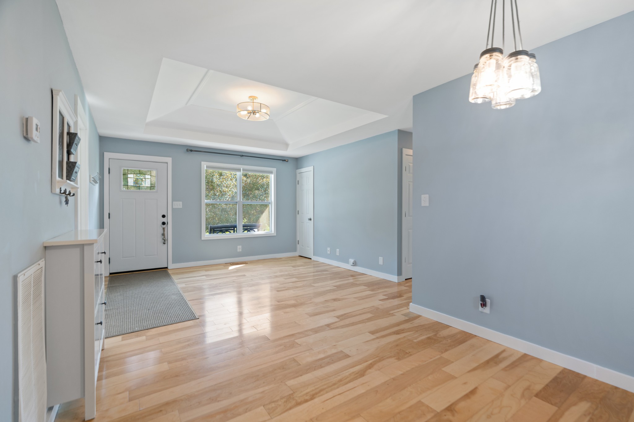 Bright living and entry area with pale blue walls, hardwood floors, and a tray ceiling.