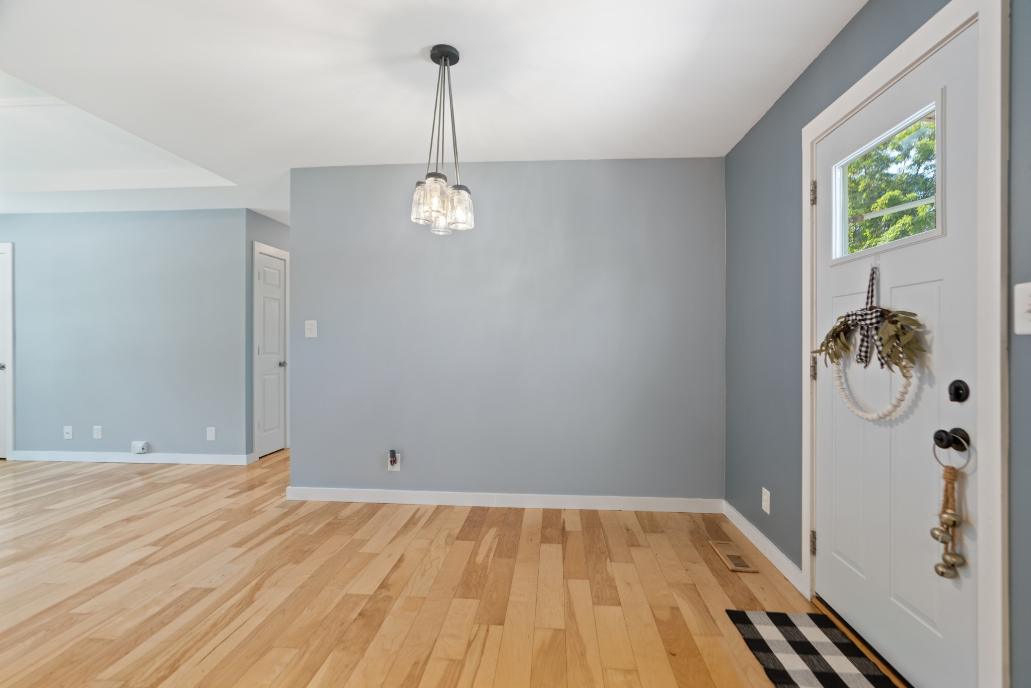 Entryway with light hardwood floors, gray walls, and a white front door with a wreath.