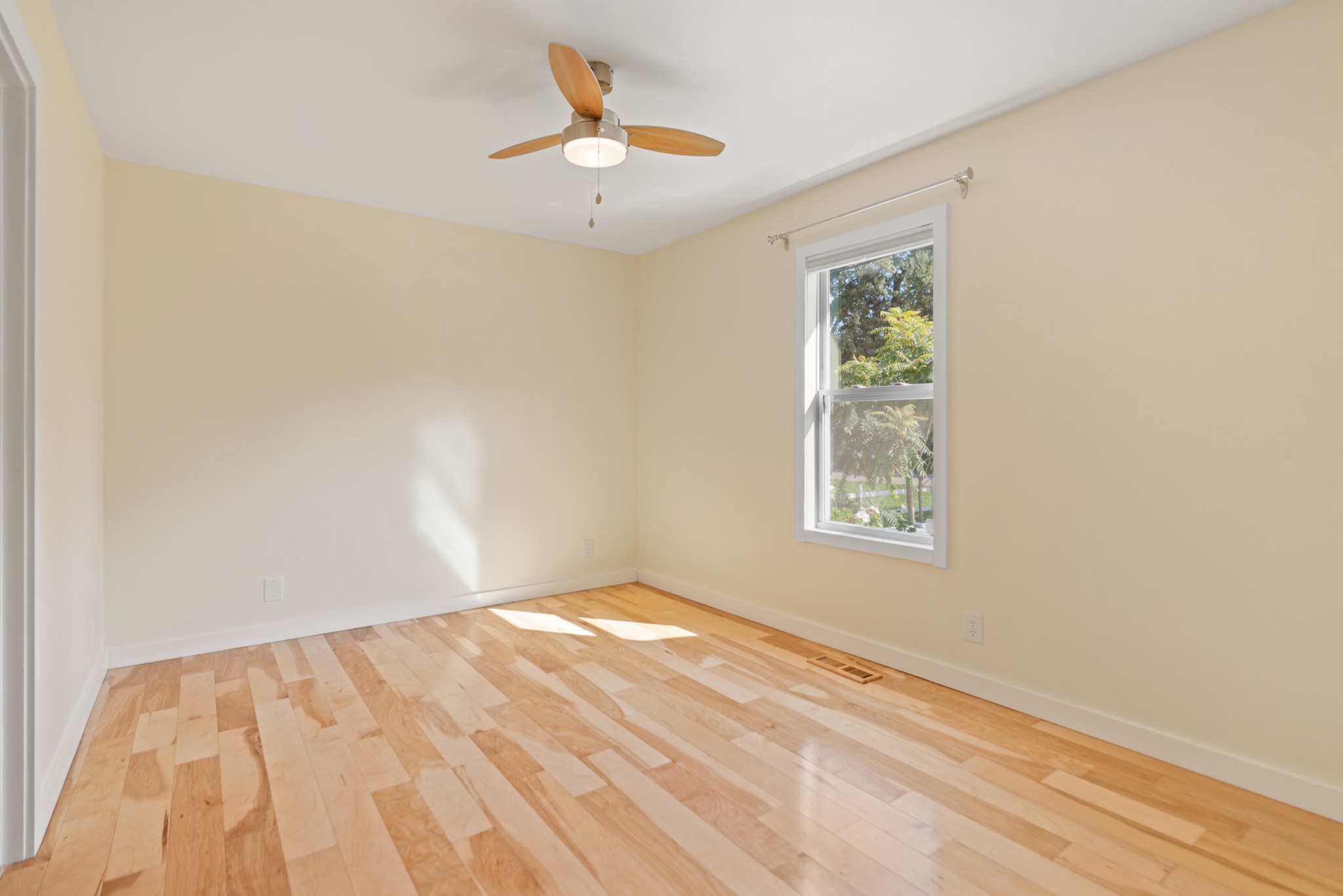 Empty room with light hardwood floors, a white-trimmed window, and a wood-blade ceiling fan.