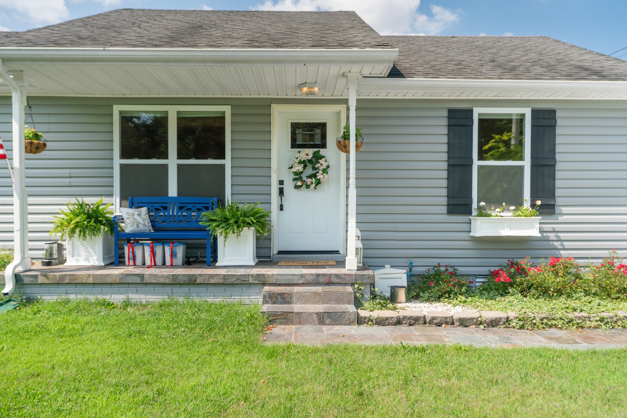 Gray-sided home with a covered front porch, blue bench, and stone steps.