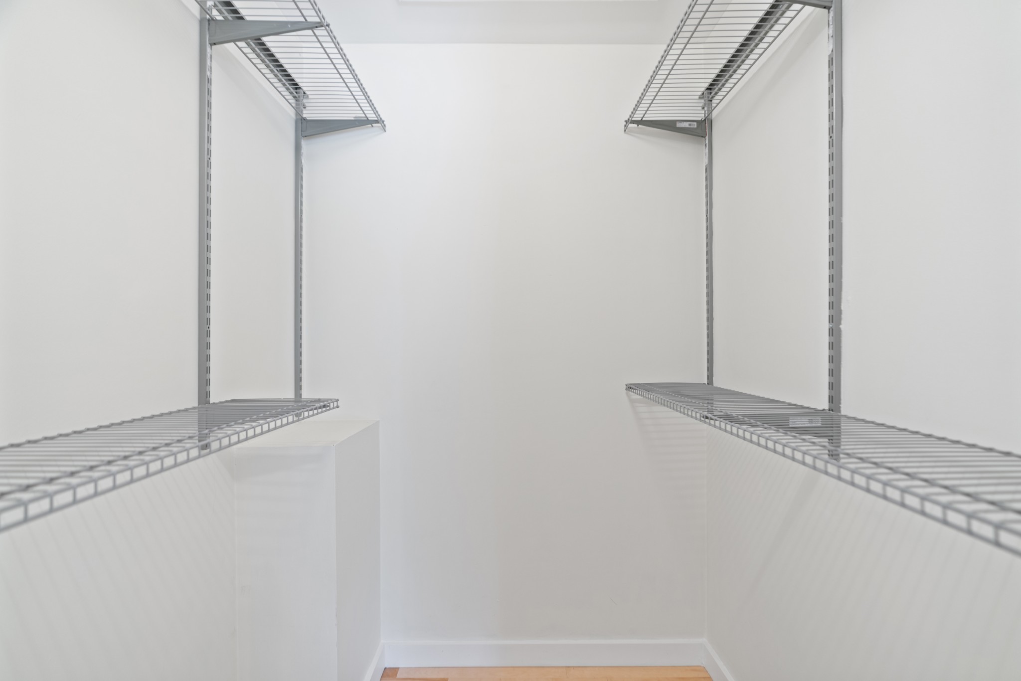 Walk-in closet with wire shelving on both sides and light wood flooring.