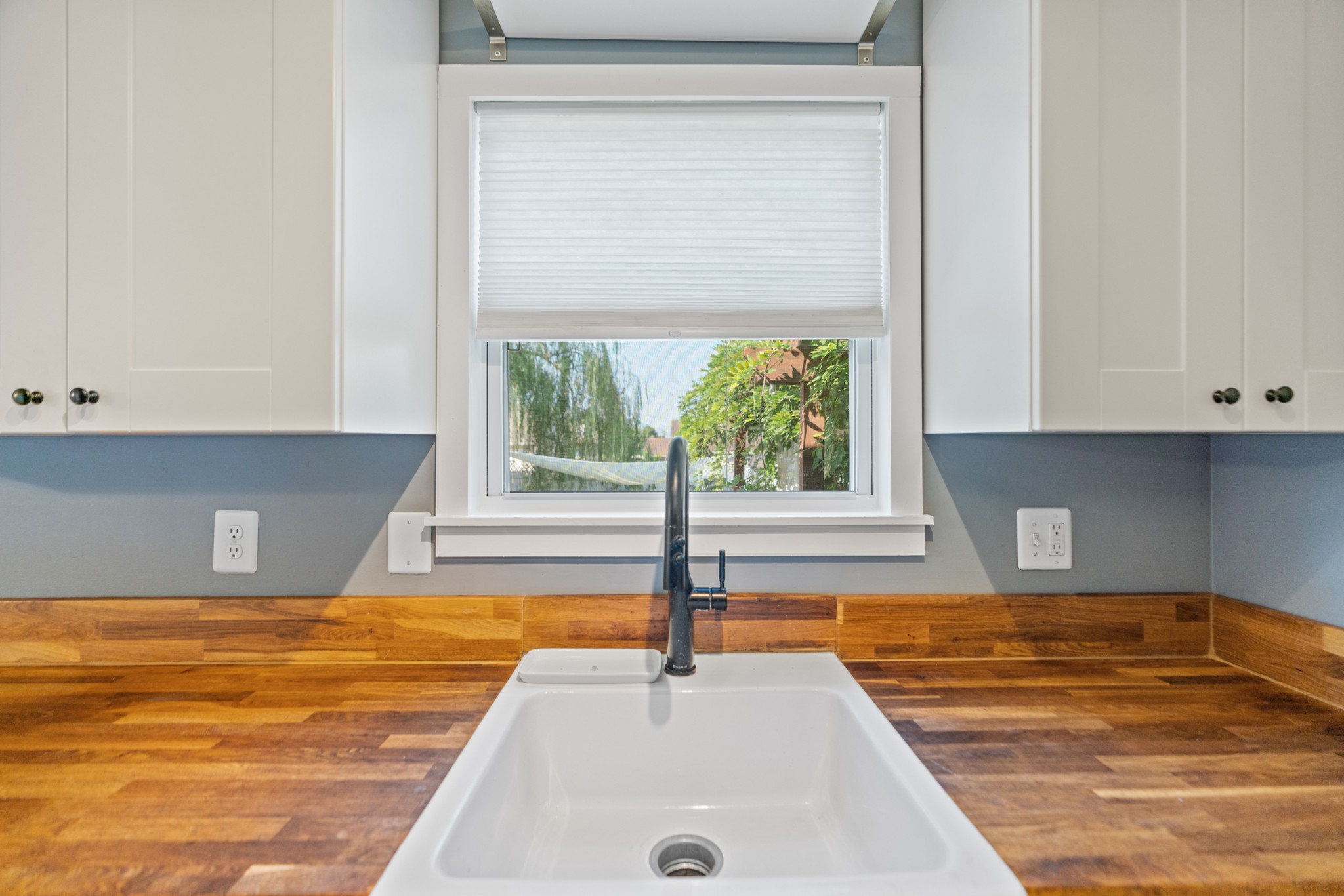 Kitchen sink with butcher-block counters, white cabinets, and a window overlooking greenery.