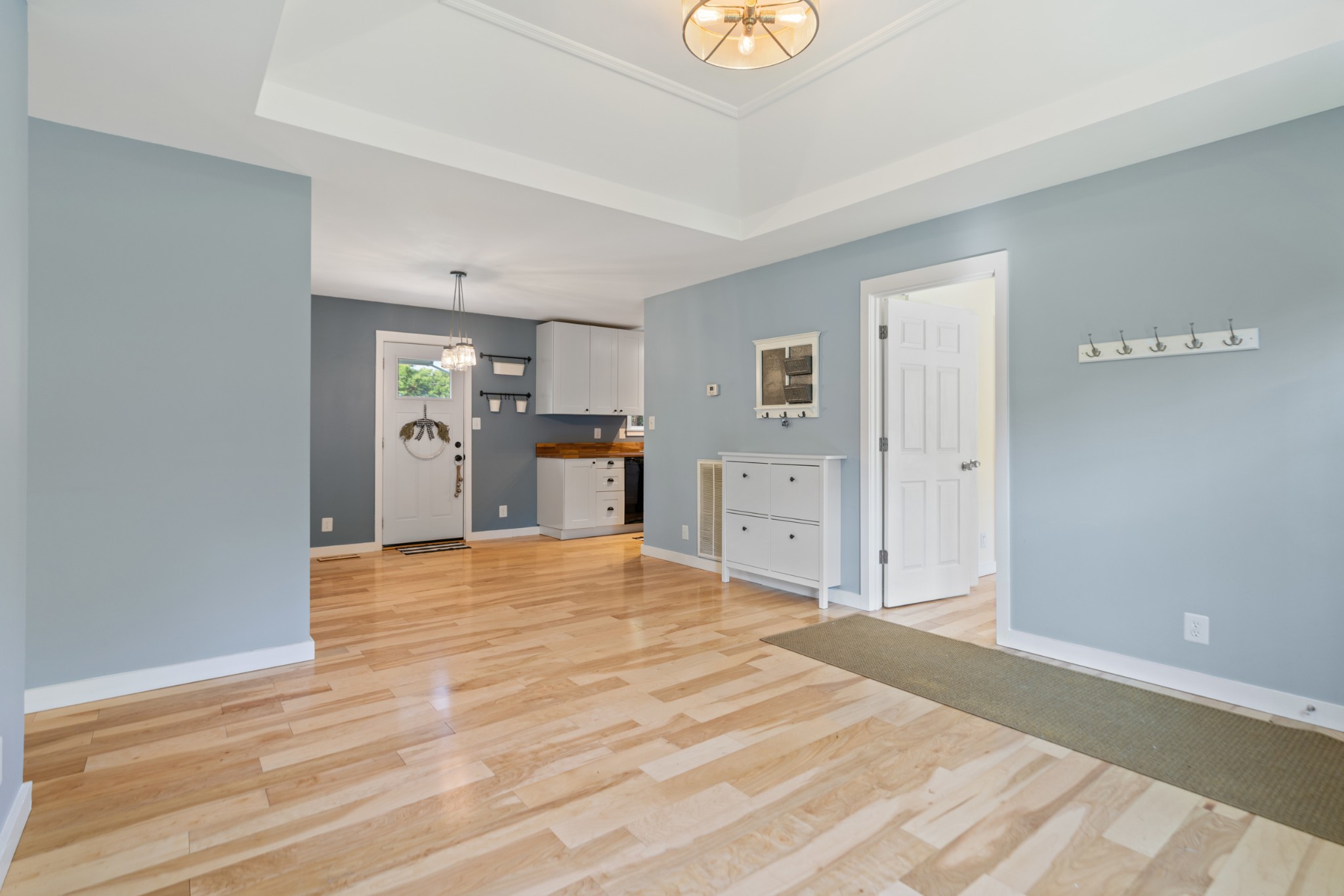 Entryway with light wood floors, blue walls, and a view into the kitchen.
