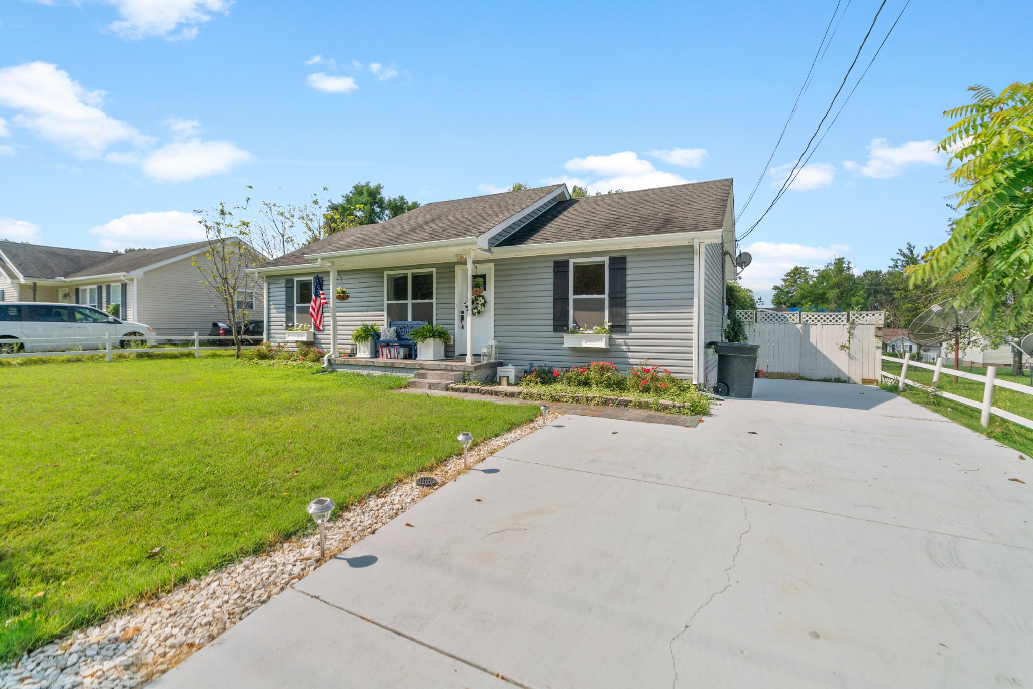 Gray single-story house with a covered porch, landscaped lawn, and wide concrete driveway.