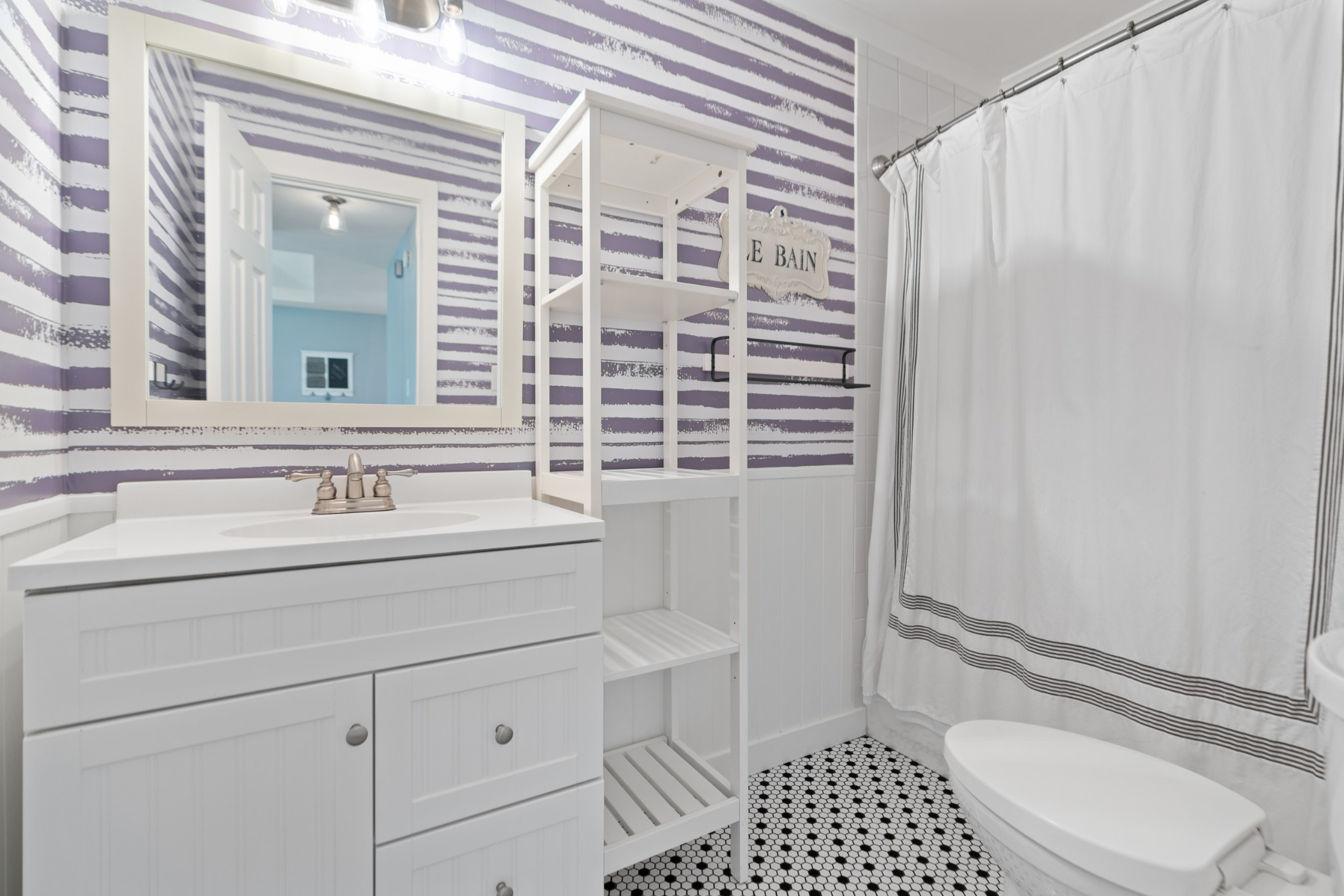 Bathroom with purple-and-white striped walls, white vanity, open shelving, and black-and-white hexagonal tile.