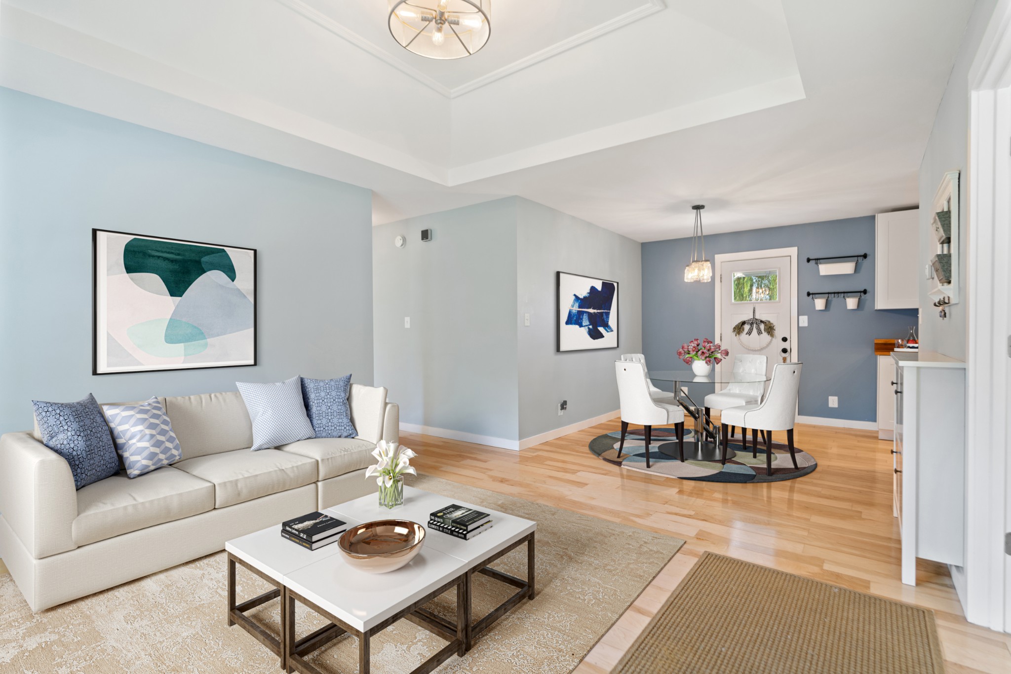 Open-plan living and dining room with a white sofa, glass dining table, and light hardwood floors.