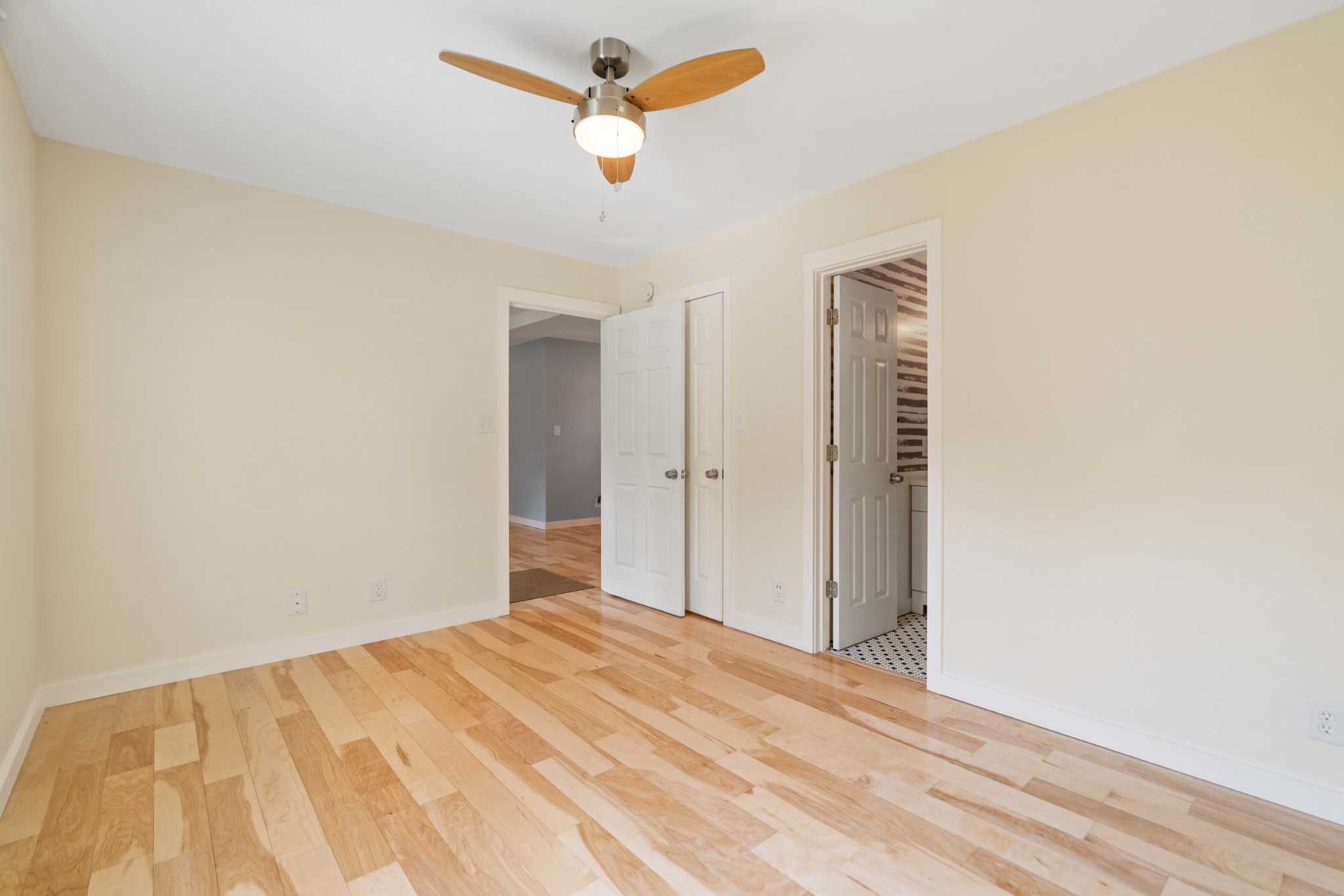 Empty bedroom with hardwood floors, a wood-blade ceiling fan, and open doors to adjoining rooms.