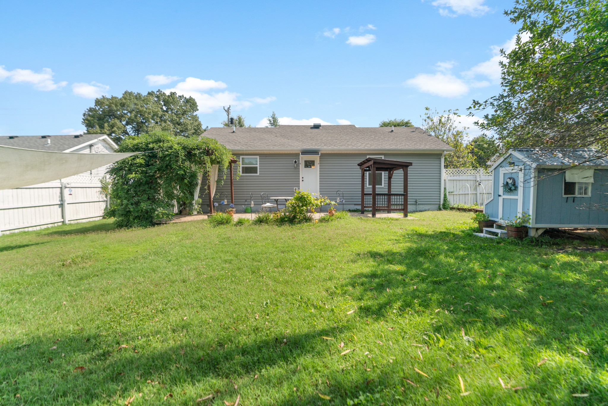 Gray house overlooking a fenced grassy backyard with a wooden gazebo and blue garden shed.
