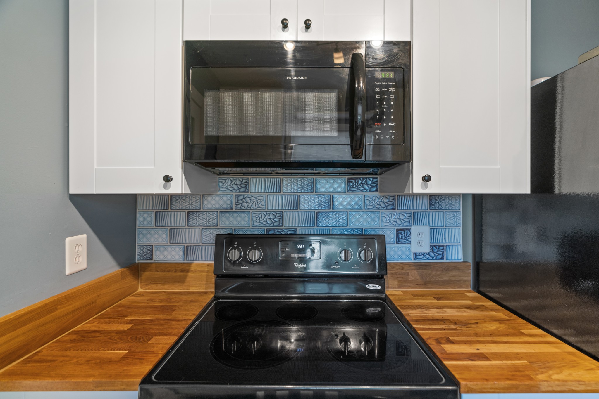 Kitchen range and microwave against a blue patterned tile backsplash, with butcher-block countertops.